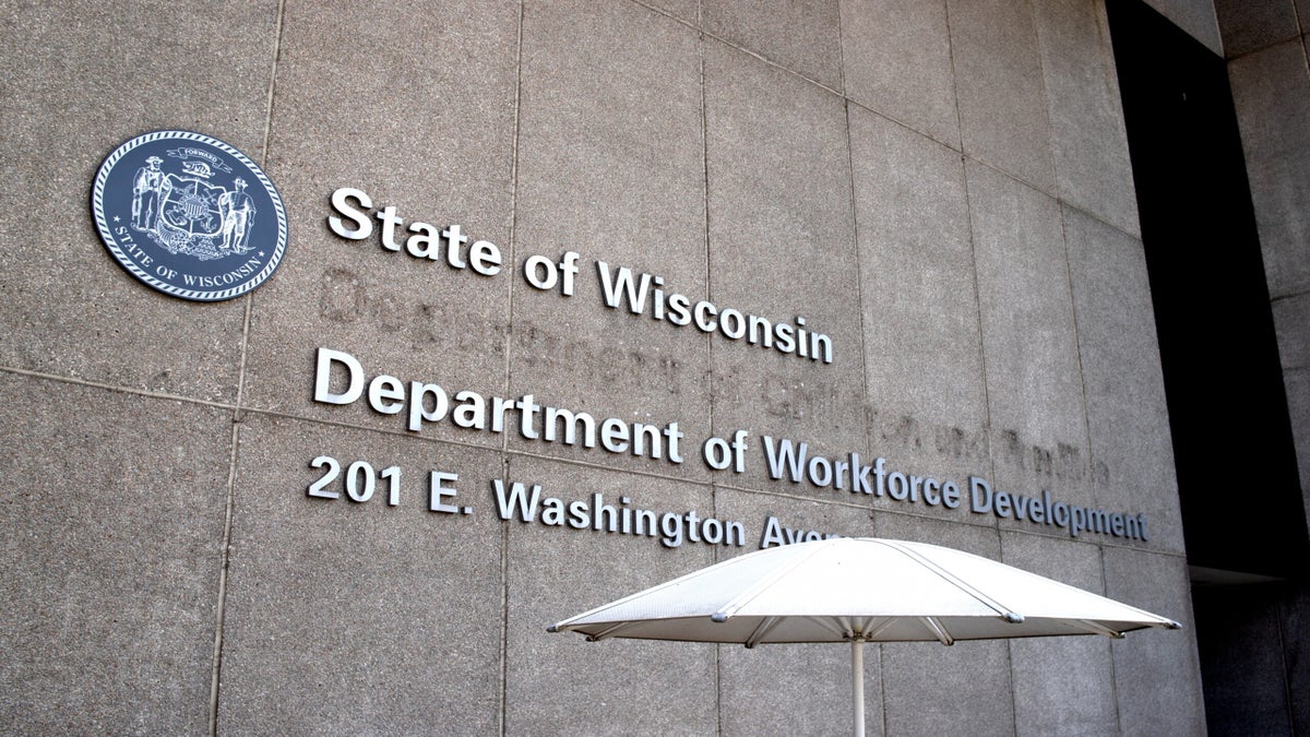 Building exterior with State of Wisconsin Department of Workforce Development, 201 E. Washington Avenue sign and state seal, partially shaded by a white umbrella.