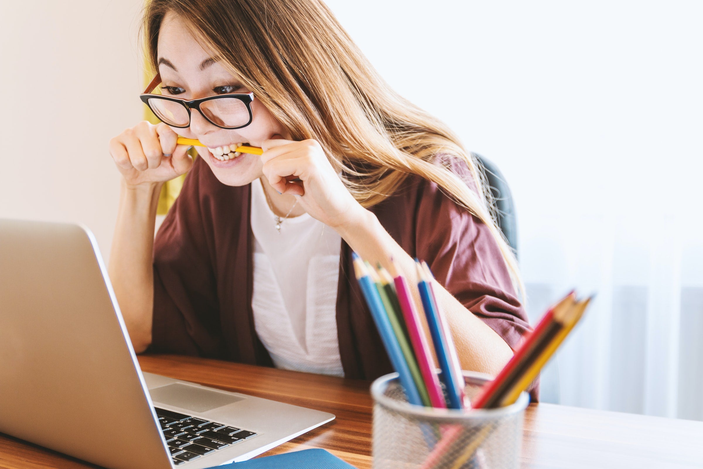 A woman biting on a pencil in front of a computer