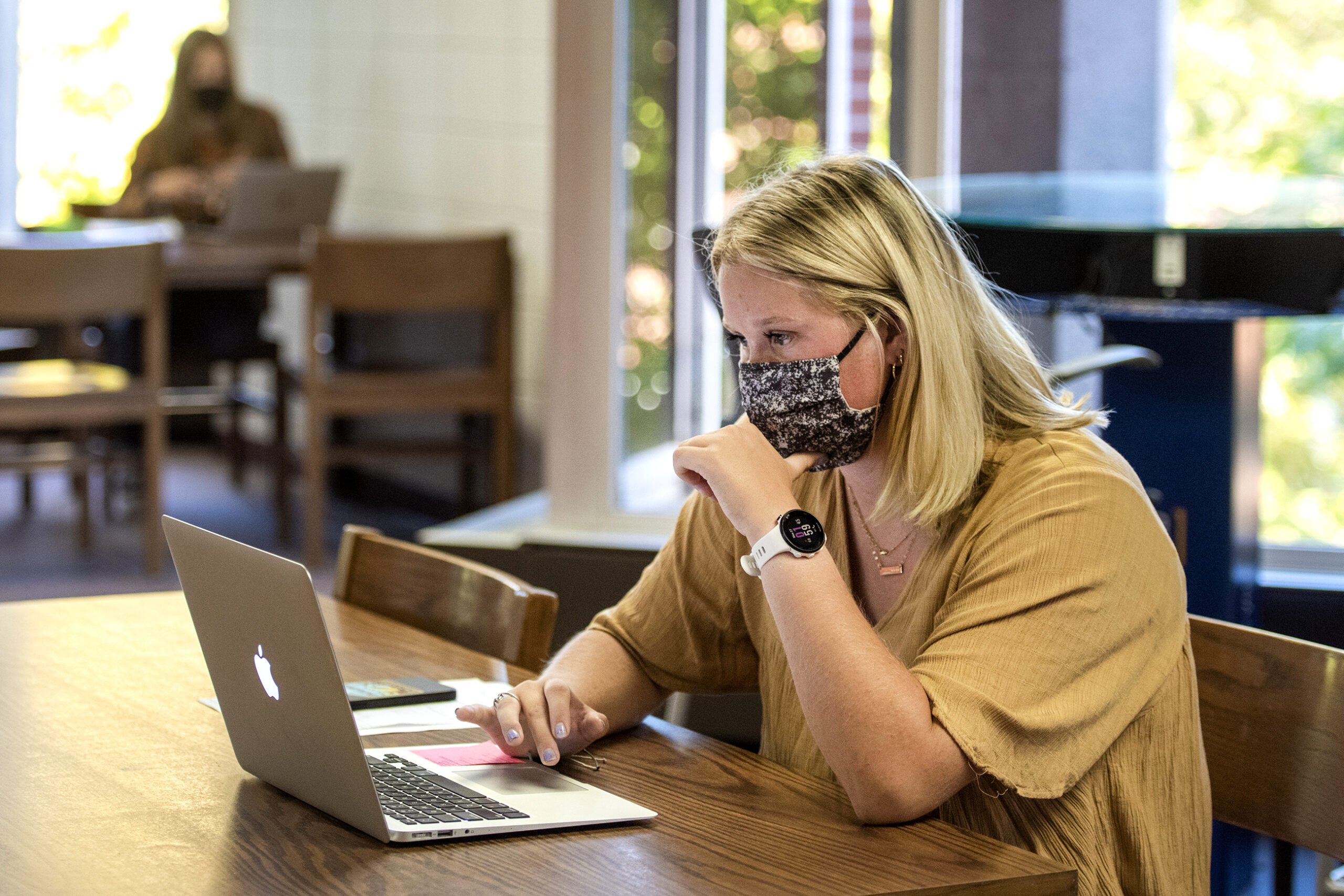 A student wears a face mask as she works on a laptop in the library.