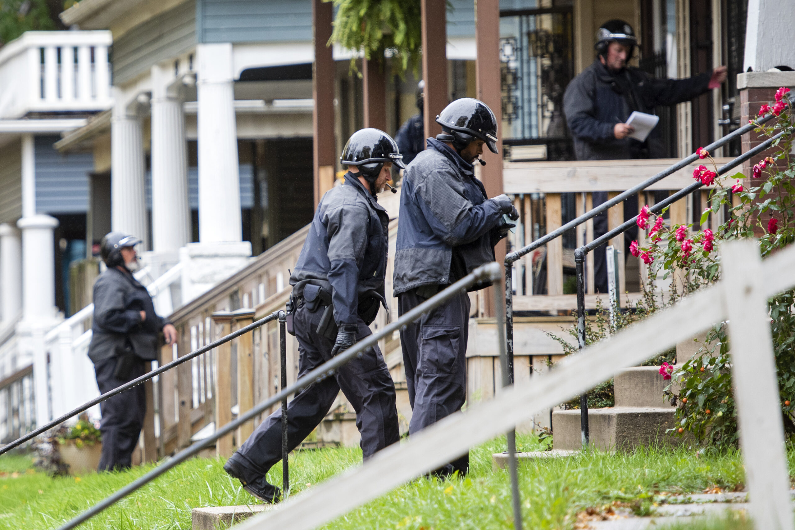 Officers in uniform climb steps to reach the front doors of homes.
