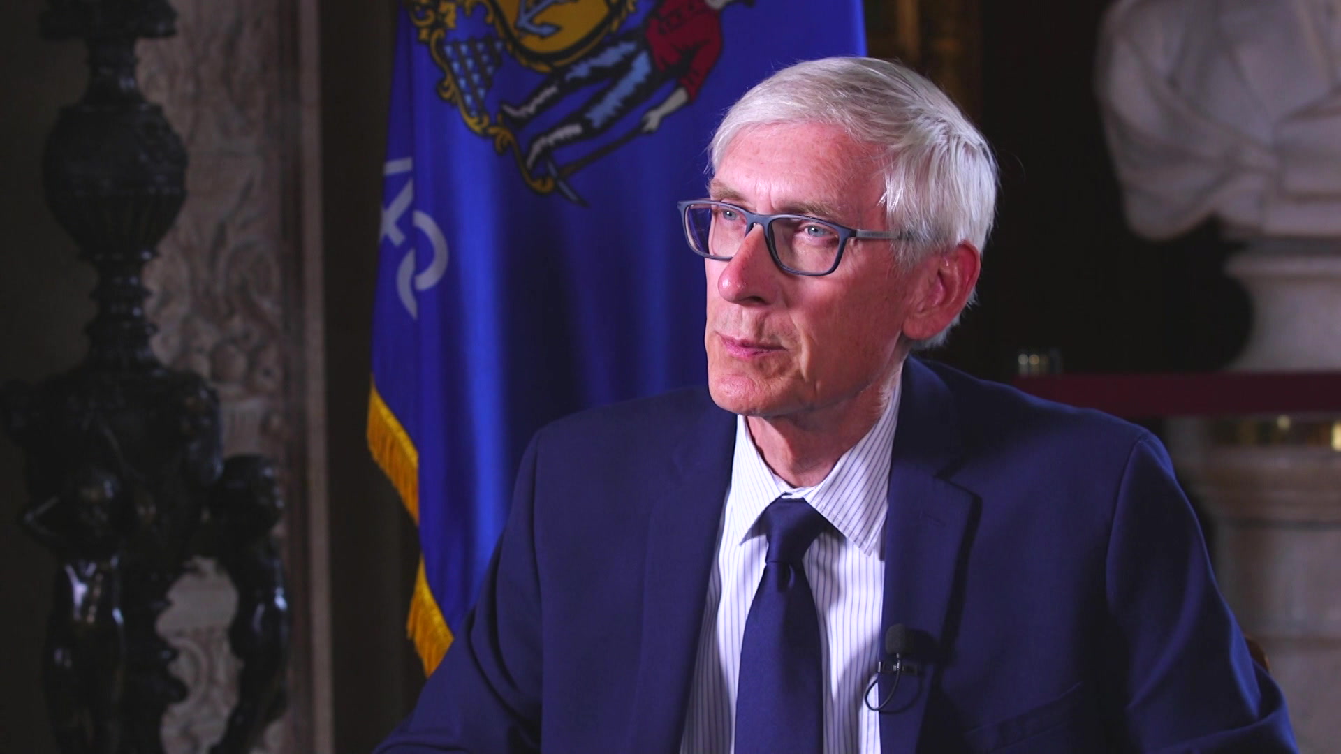 Tony Evers sits in front of a Wisconsin flag.