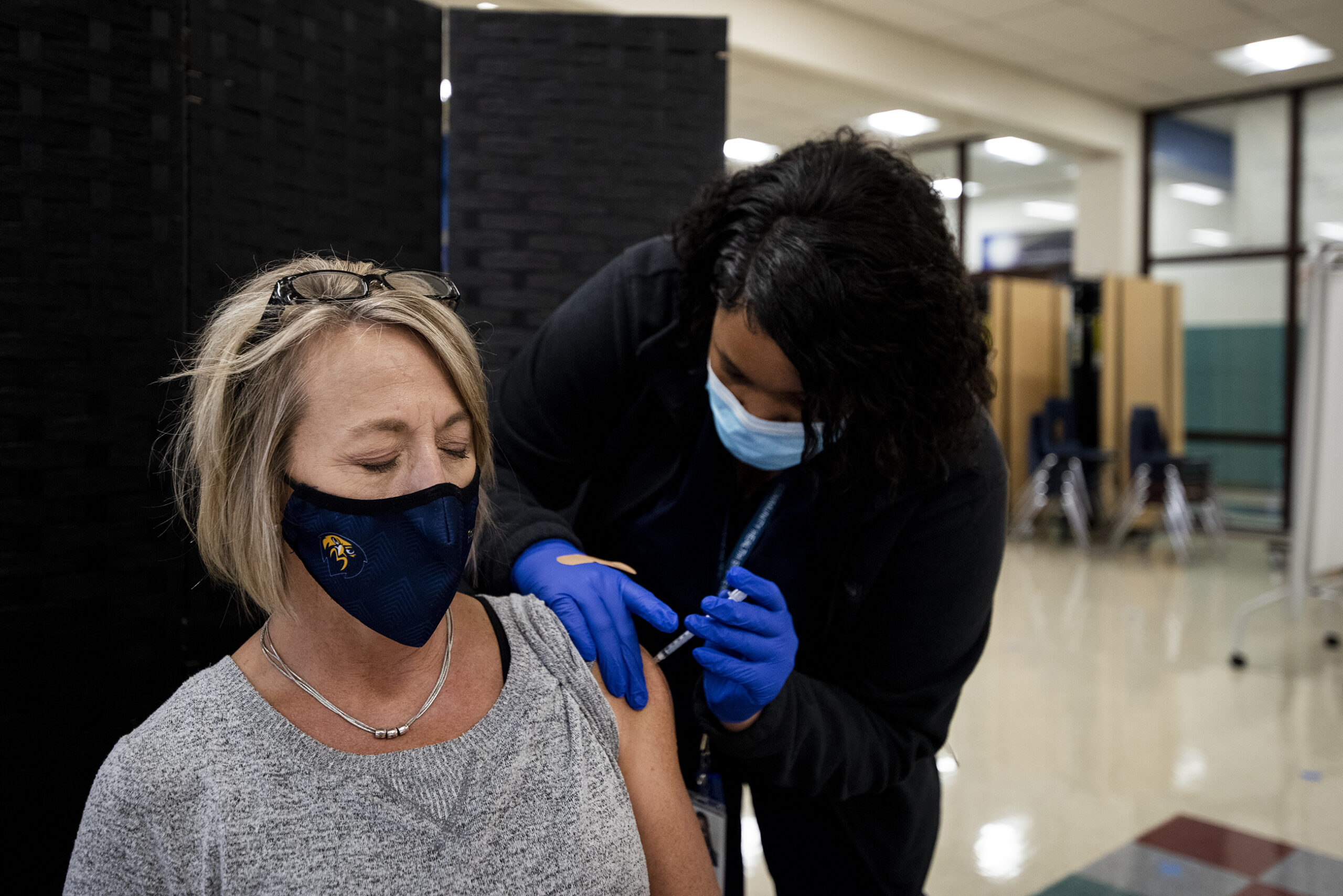A woman in a face mask closes her eyes as she receives a shot