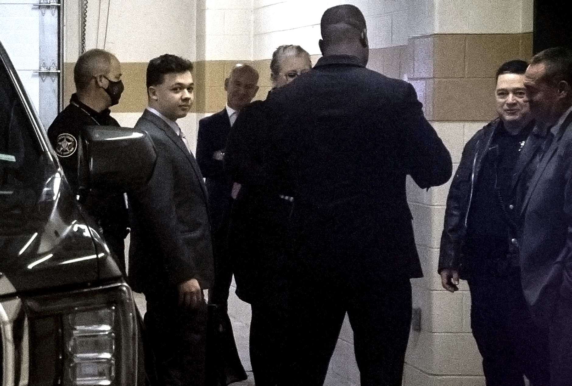 Kyle Rittenhouse is seen wearing a suit inside of a garage.