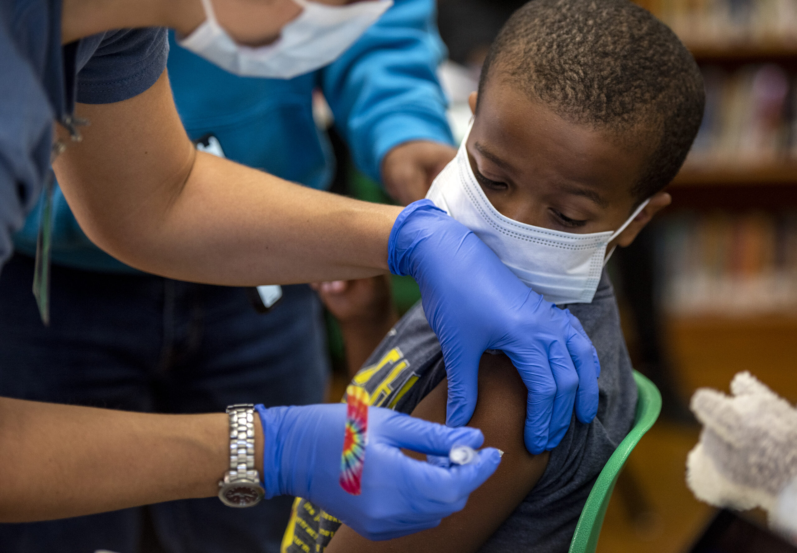 A boy wearing a face mask looks over his shoulder as he receives a shot.