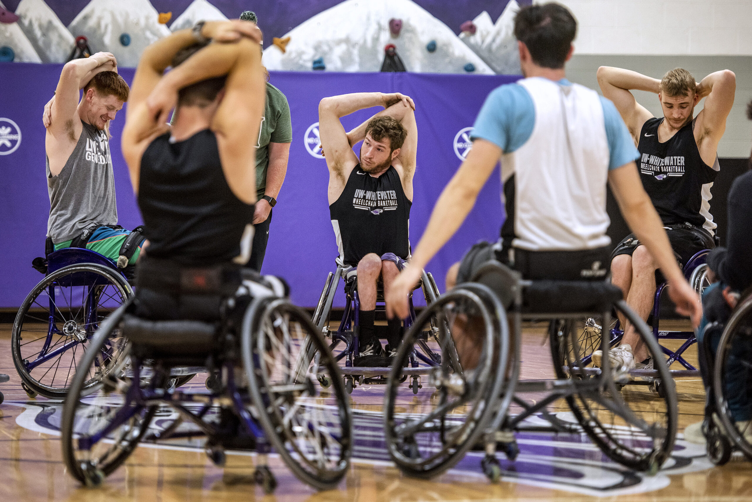 Men's wheelchair basketball players stretch their arms.