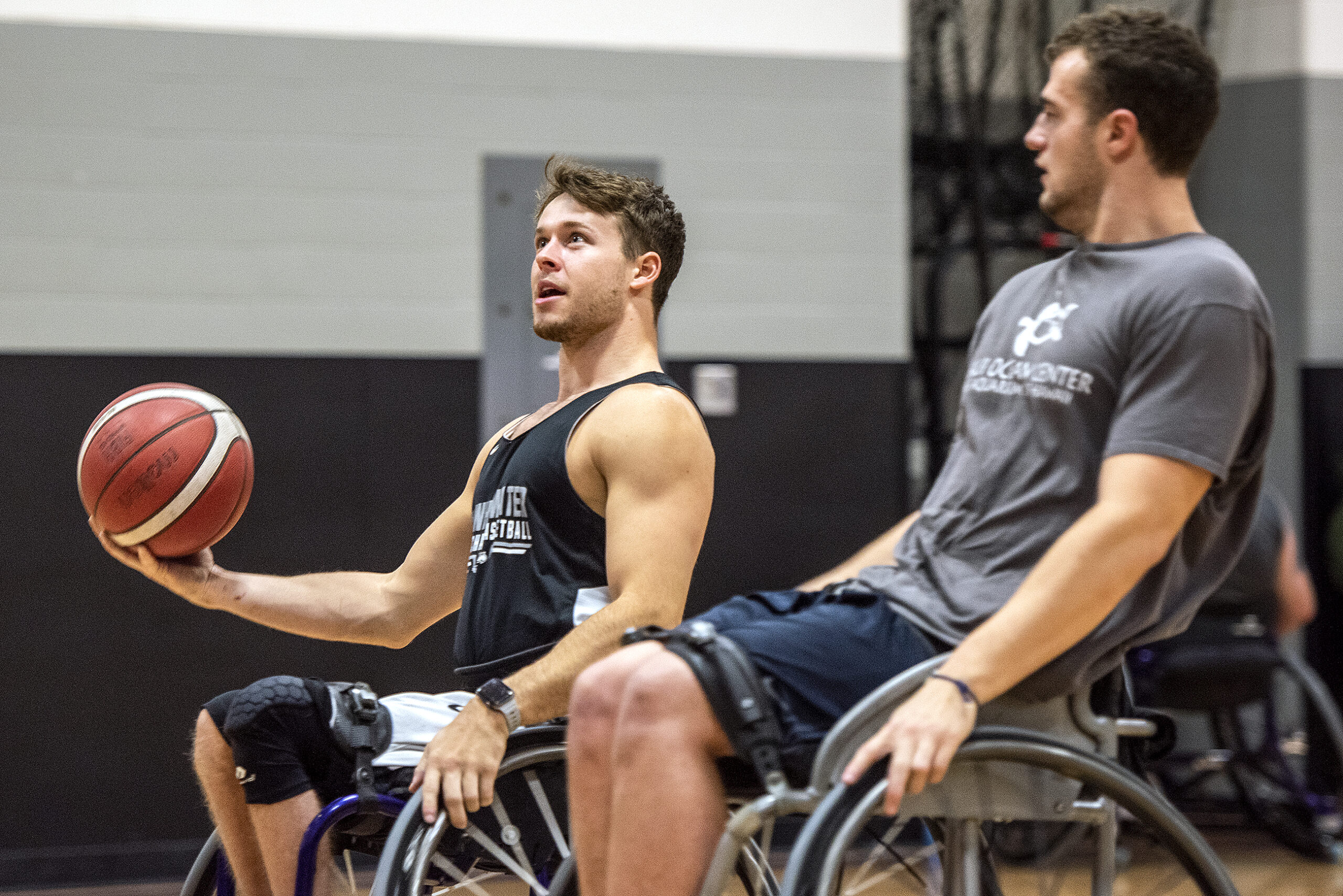 A wheelchair basketball player holds the ball in one hand as he moves toward the goal.