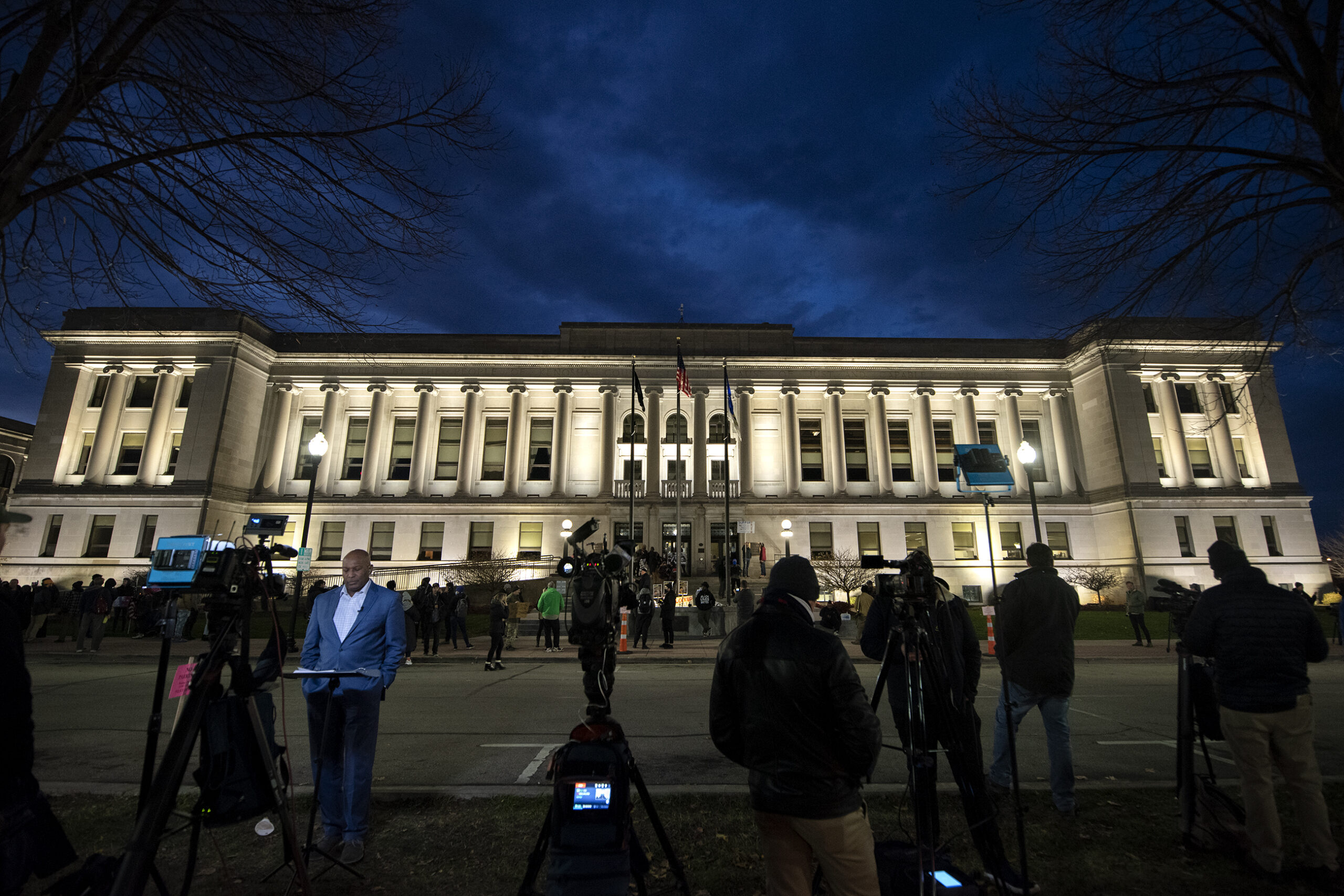 Lights illuminate the courthouse as television reporters stand in front of cameras.