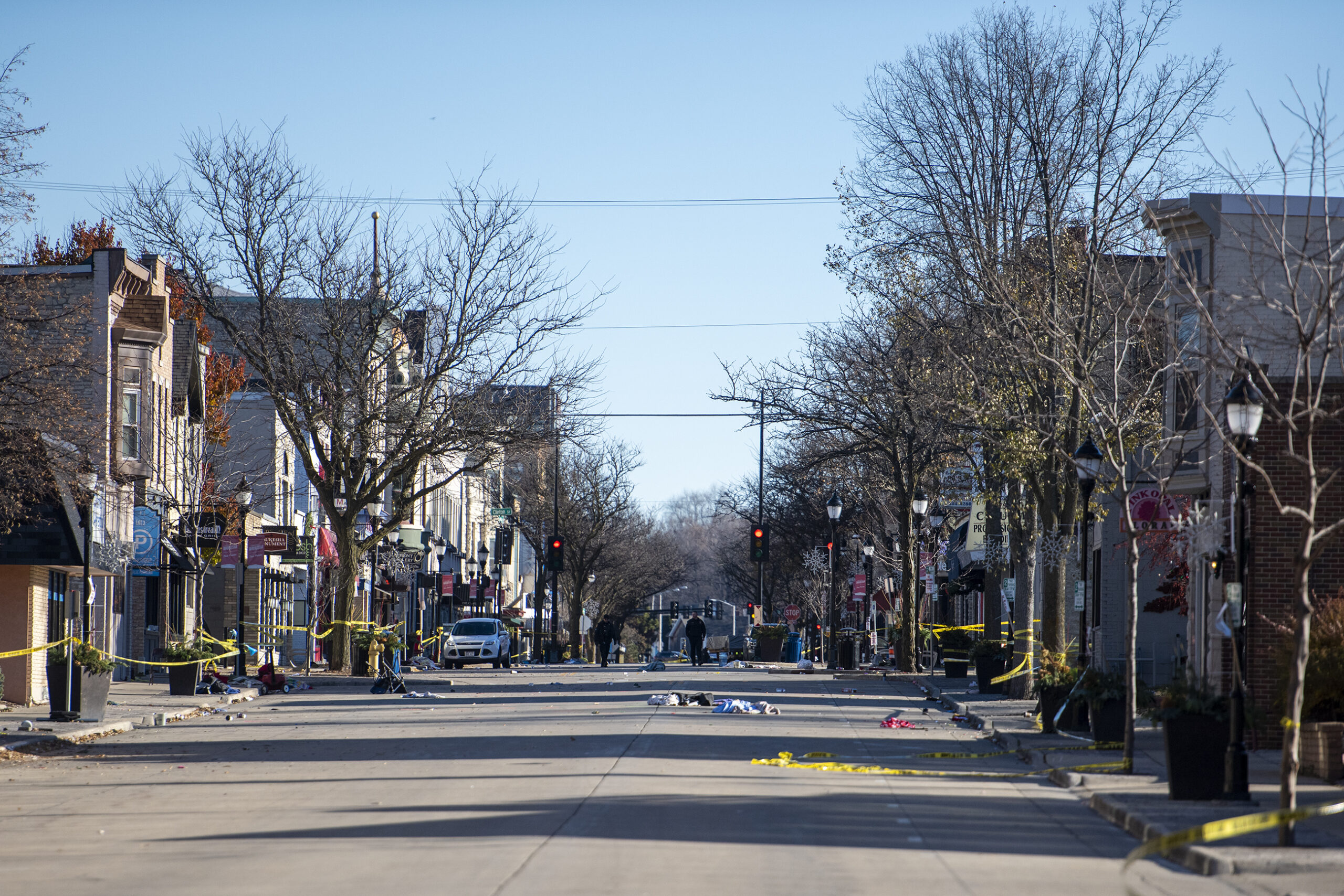 Yellow tape surrounds an empty street. Abandoned folding chairs and personal items can be seen on the side of the road.