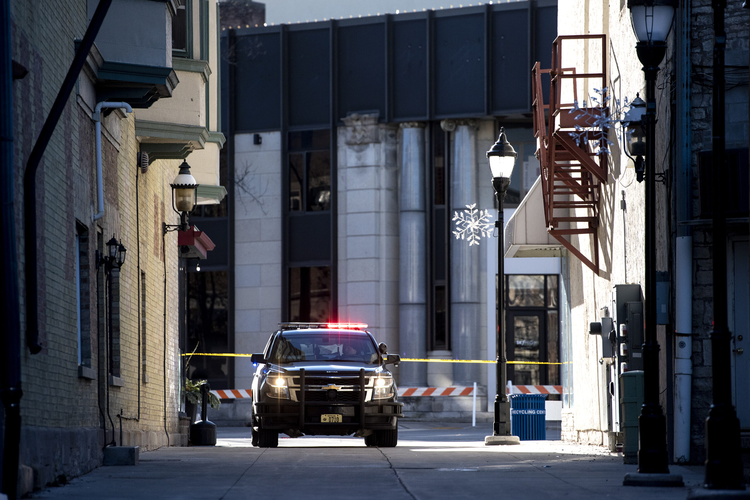 A police car with lights on is parked near yellow police tape.