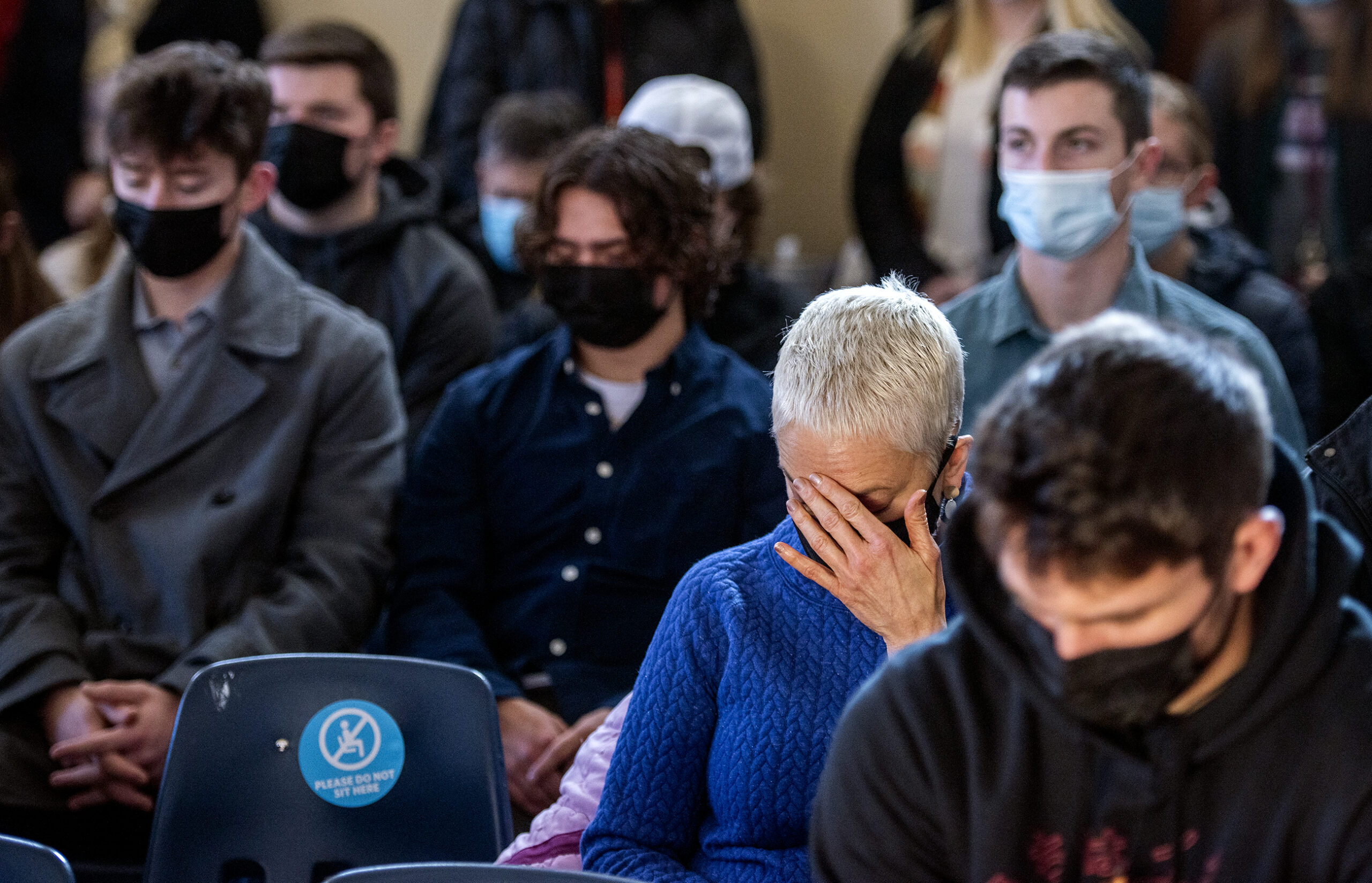 A woman a blue top covers her face with her hand as she prays with other attendees.