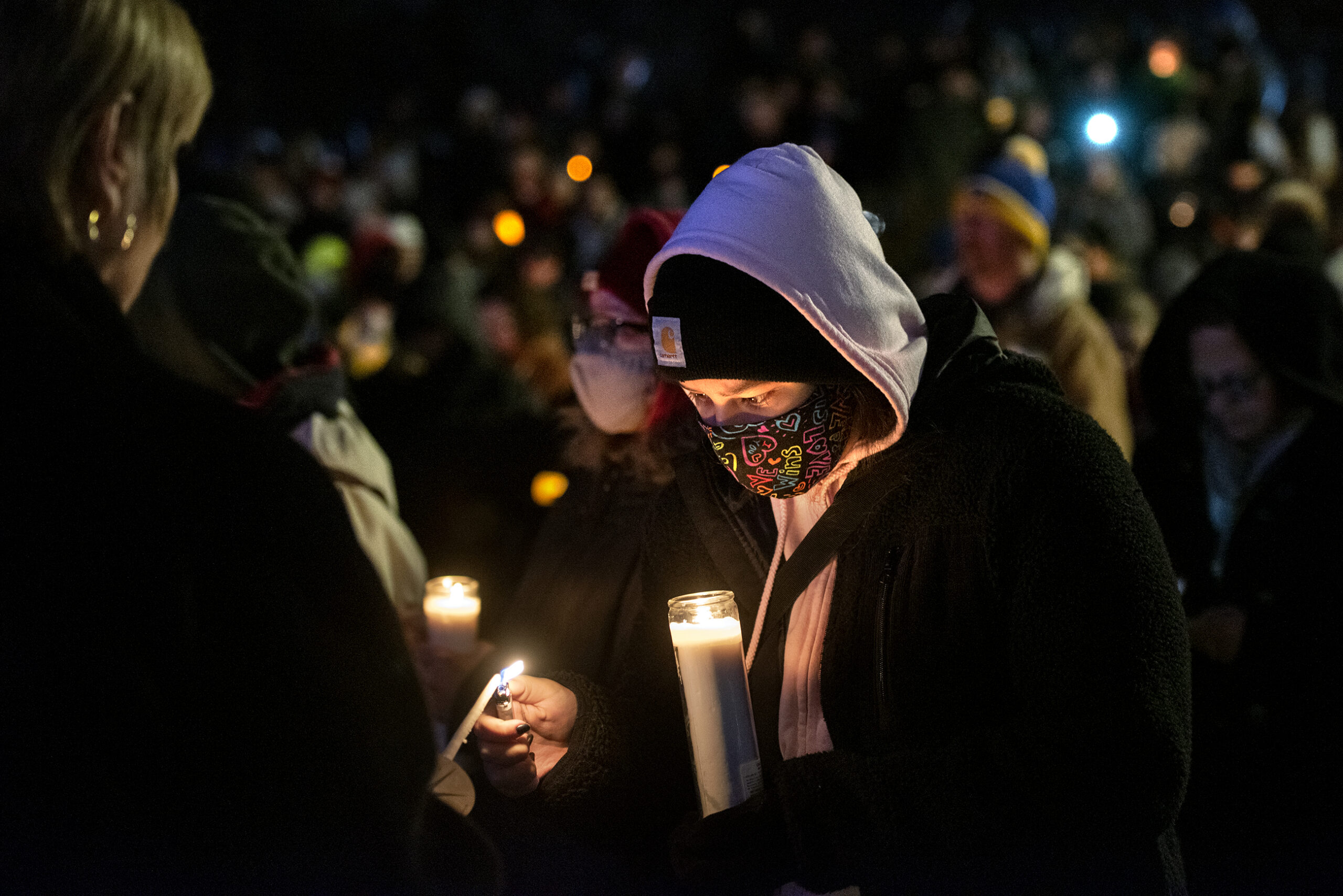 A crowd can be seen behind a woman holding a candle at night.