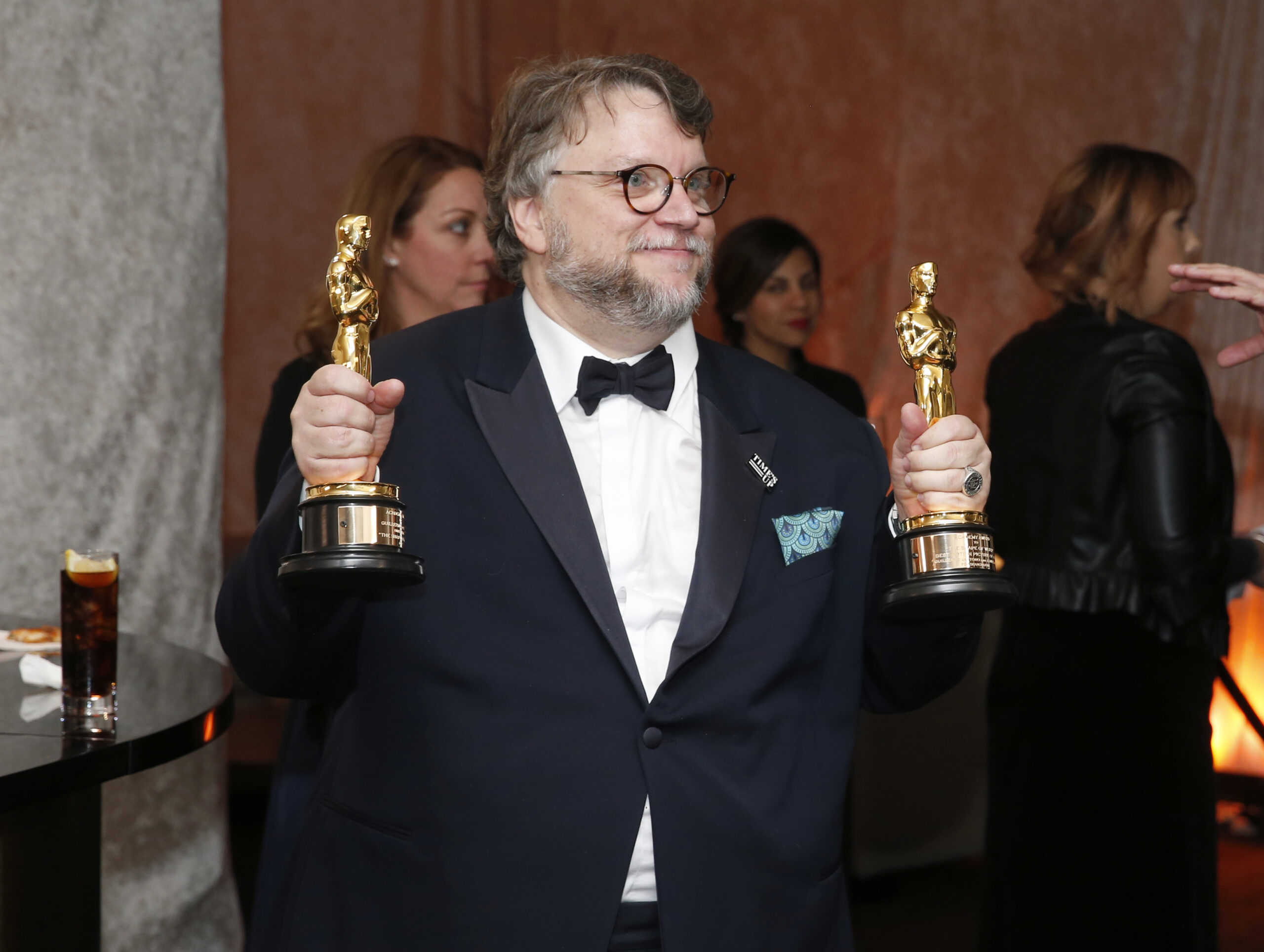 Guillermo del Toro poses holding an Academy Award in each hand