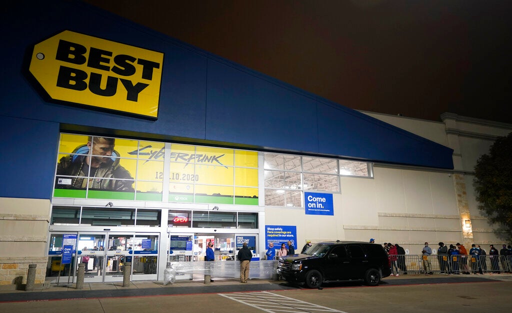 A line of people wait outside Best Buy in the dark.