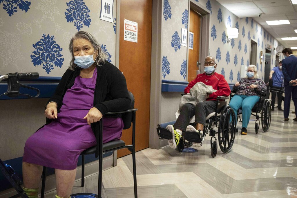Nursing home residents sit in the hallways spaced apart wearing masks.
