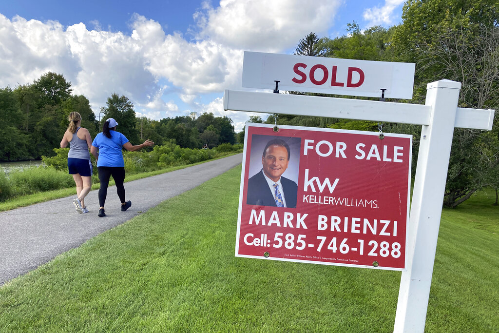 People walk by a sold sign in front of a house along the Erie Canal.