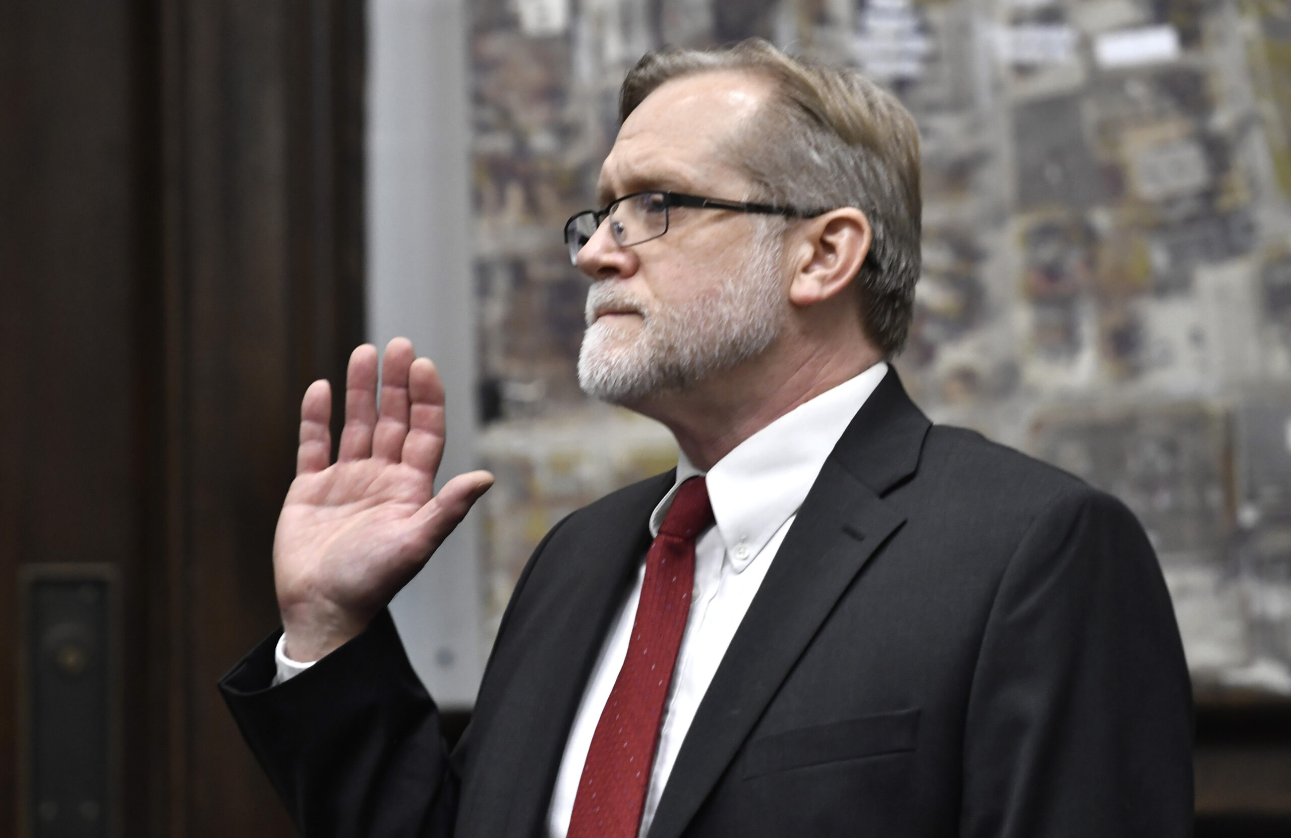 A man in a suit raises his right hand on the witness stand