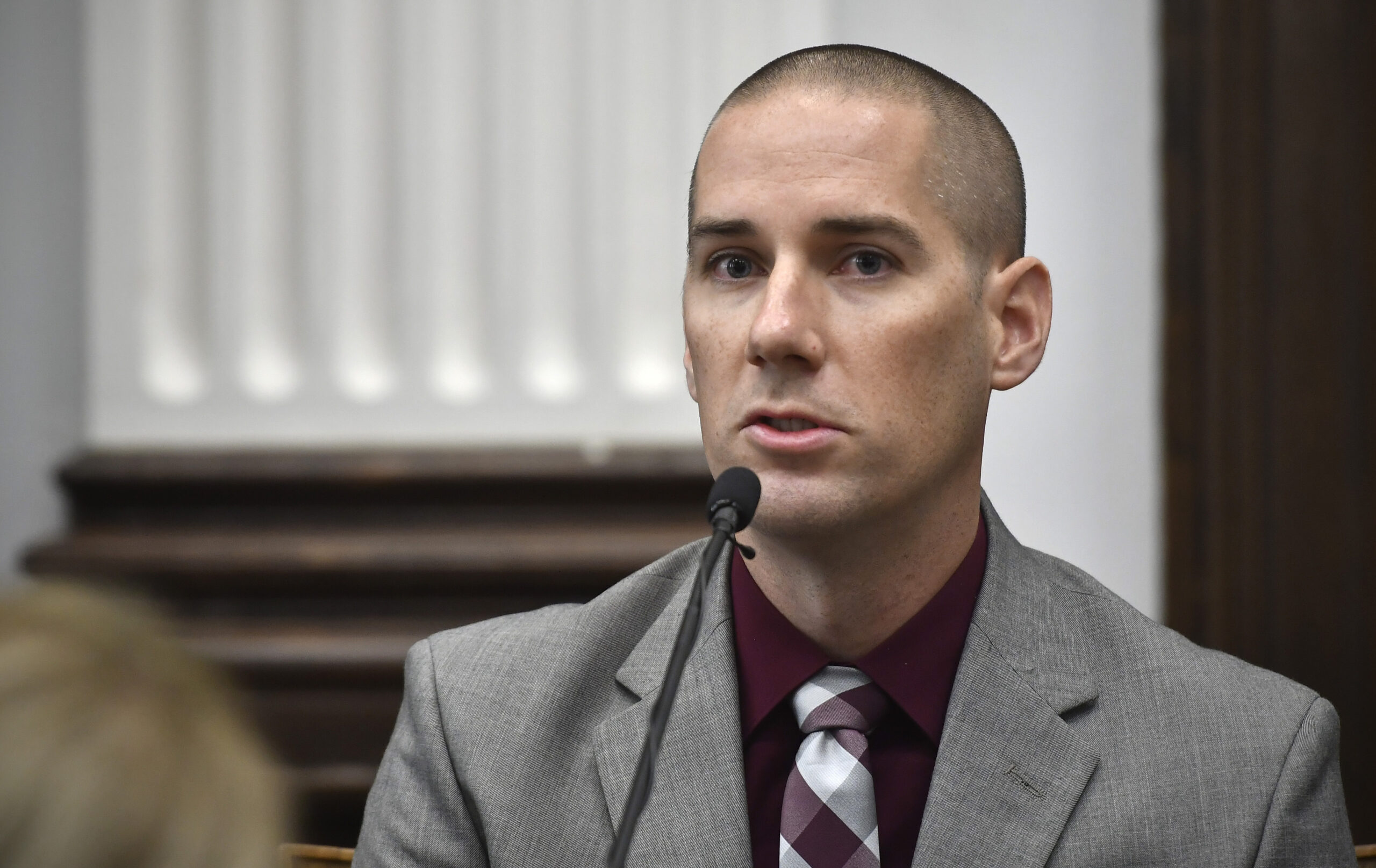 A man in a gray suit speaks into a courtroom microphone