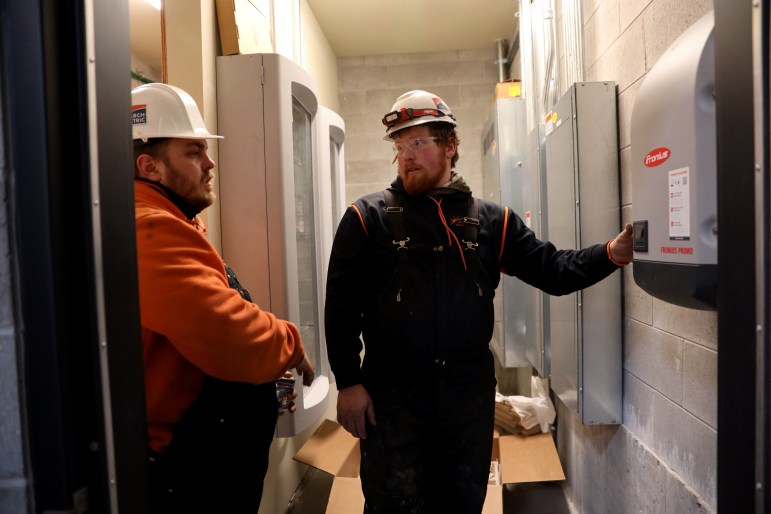 An electrician with Arch Electric helps install a solar panel inverter in an electrical room