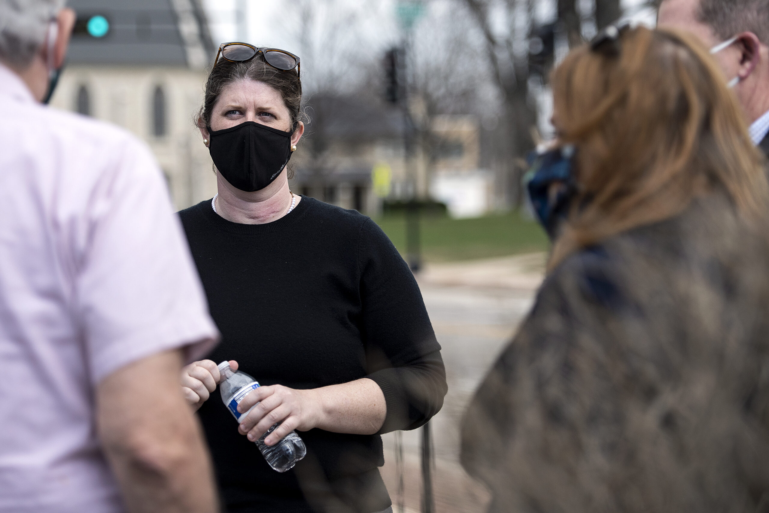 A woman in a black face mask speaks to people outside.