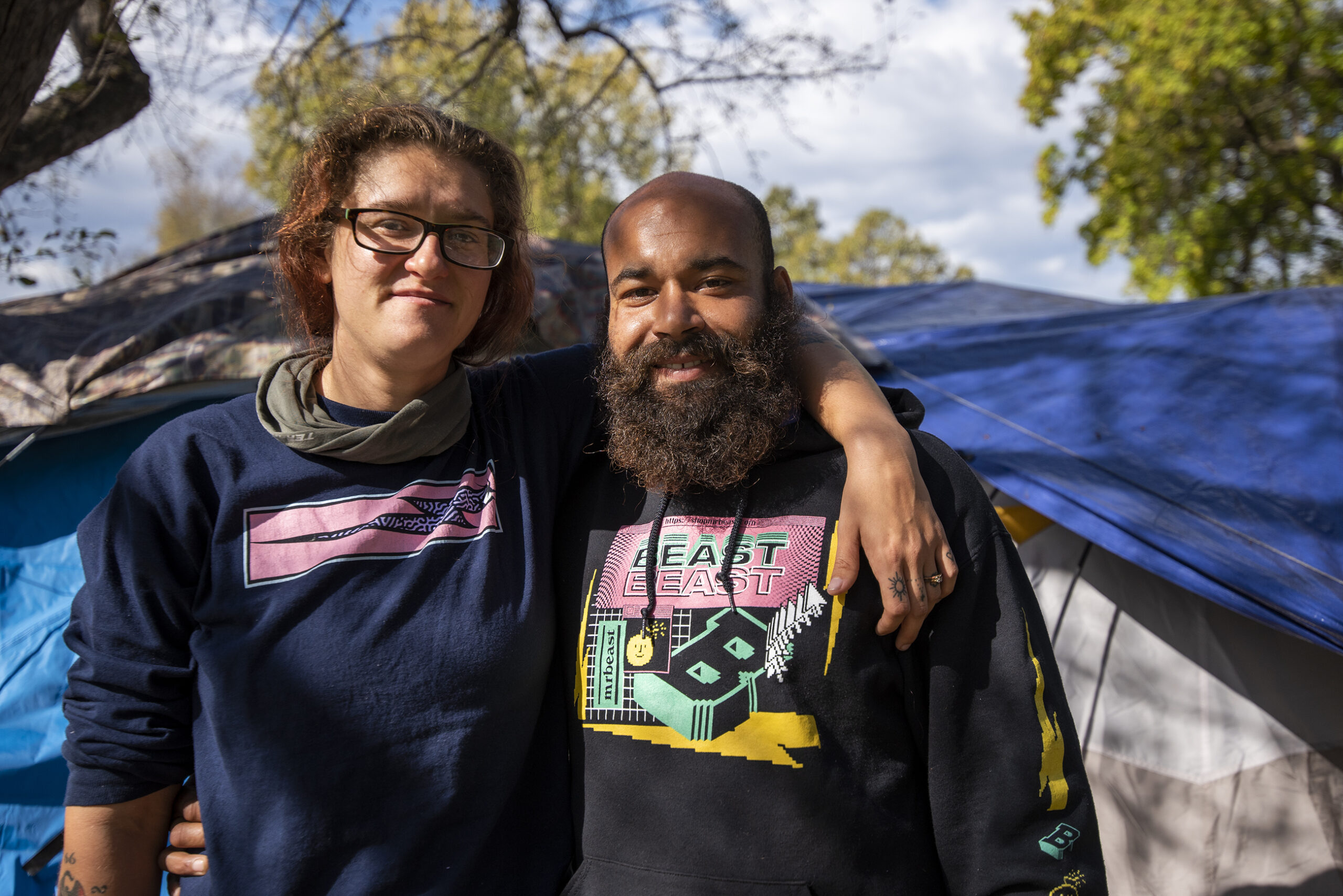 Two people stand together near the tent where they live.