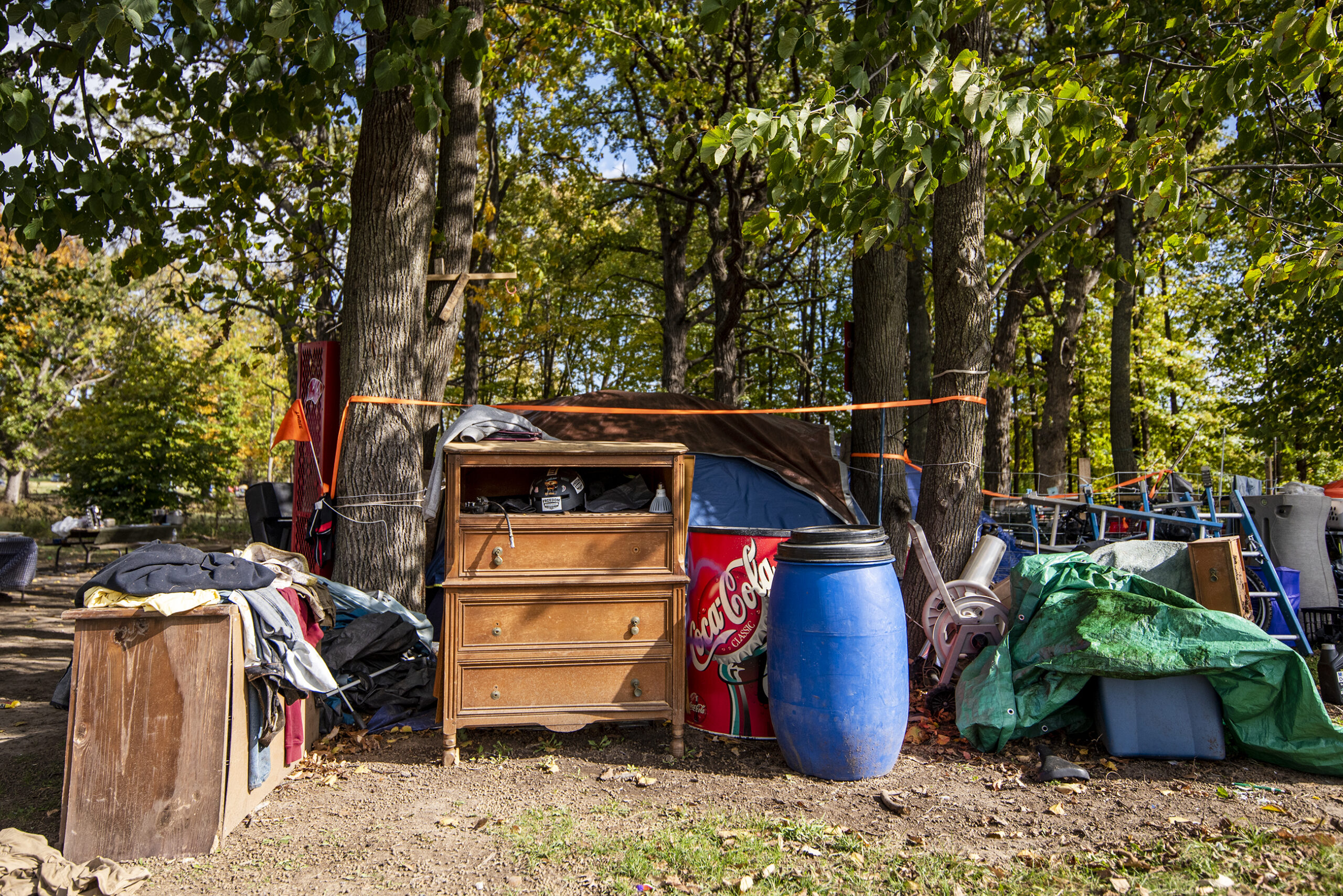 A dresser, a trash can, and other belongings are kept near trees in the park.