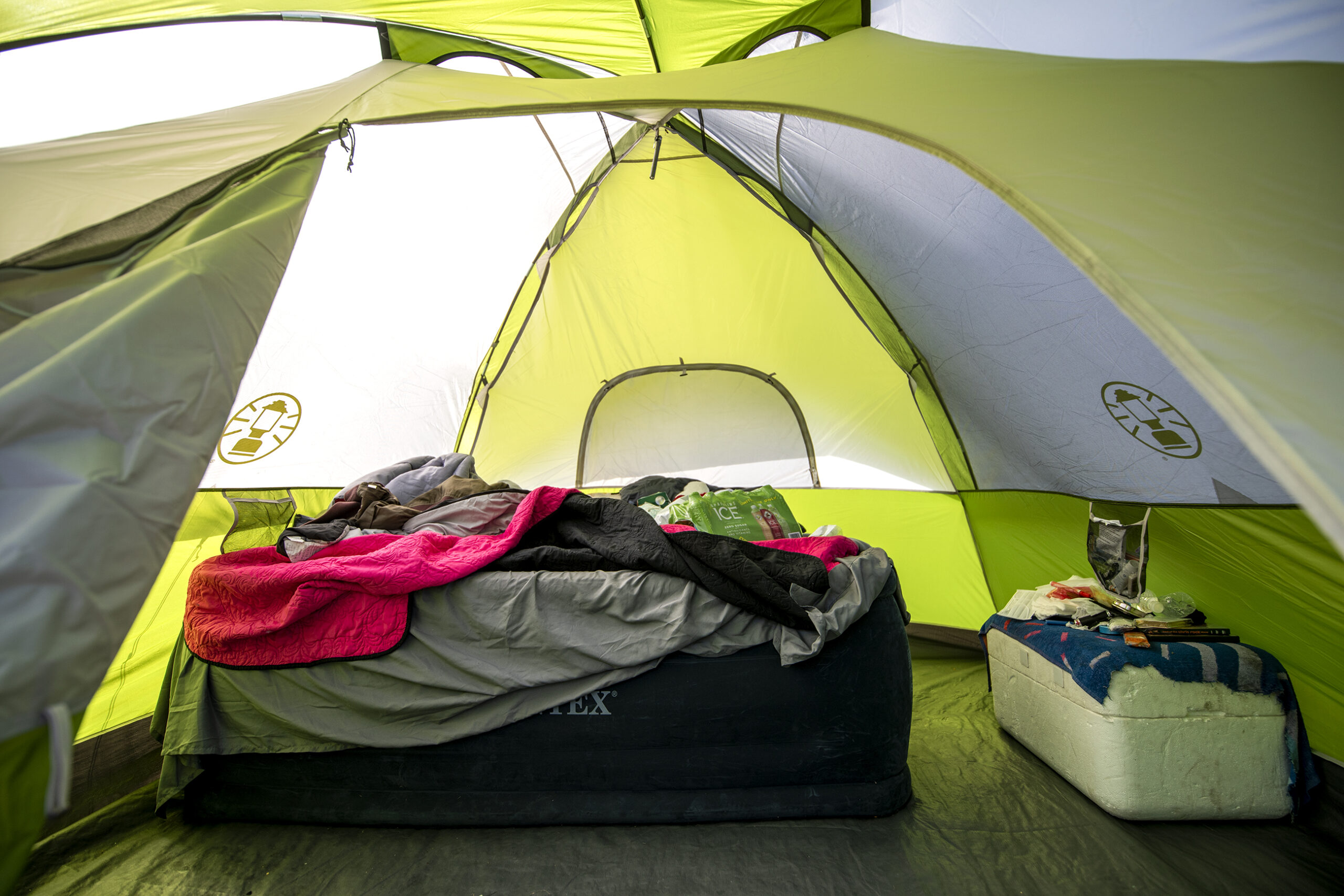 A green tent covers a bed and an ice chest.