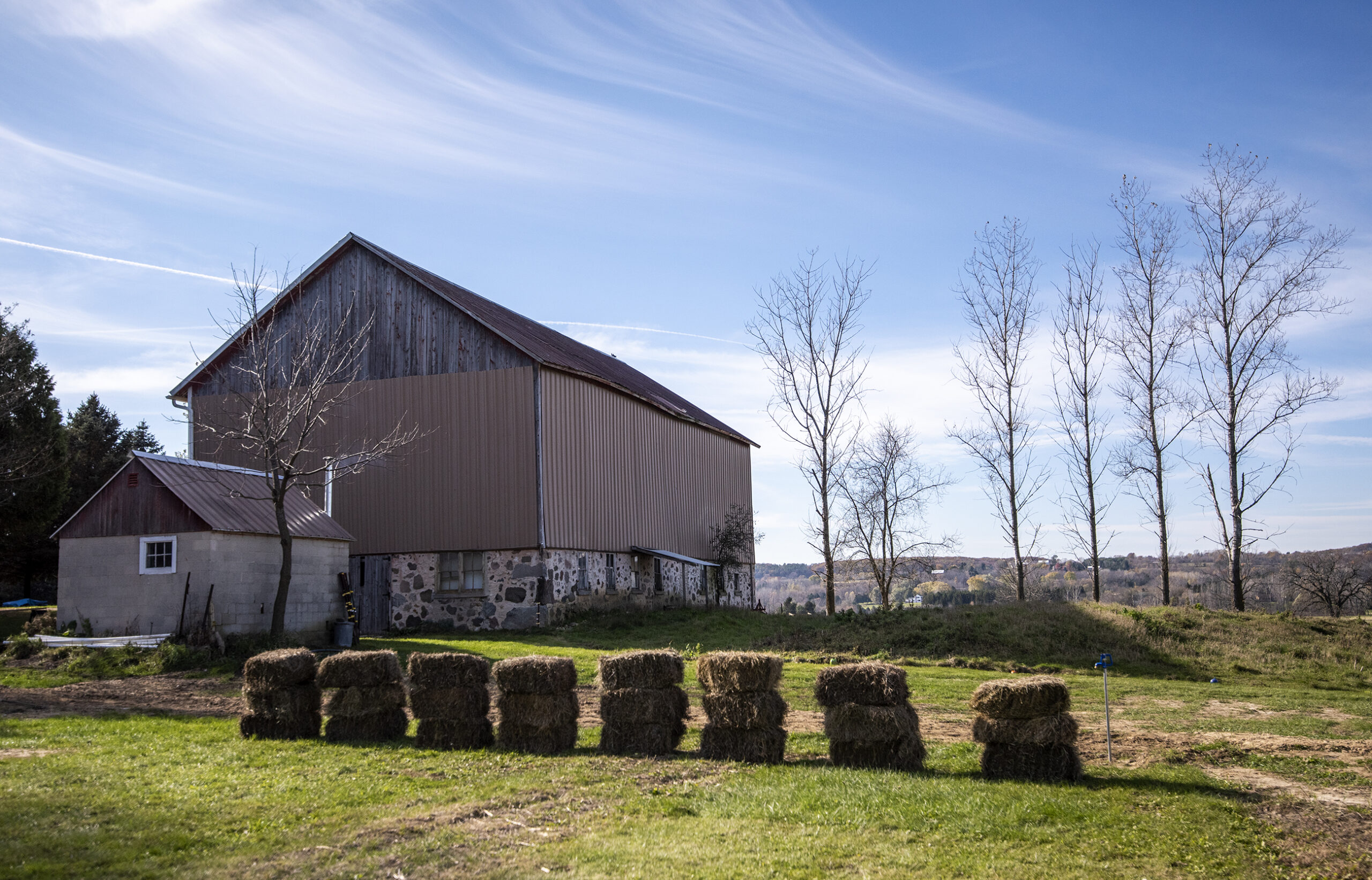 Rolling farmland can be seen behind a barn.