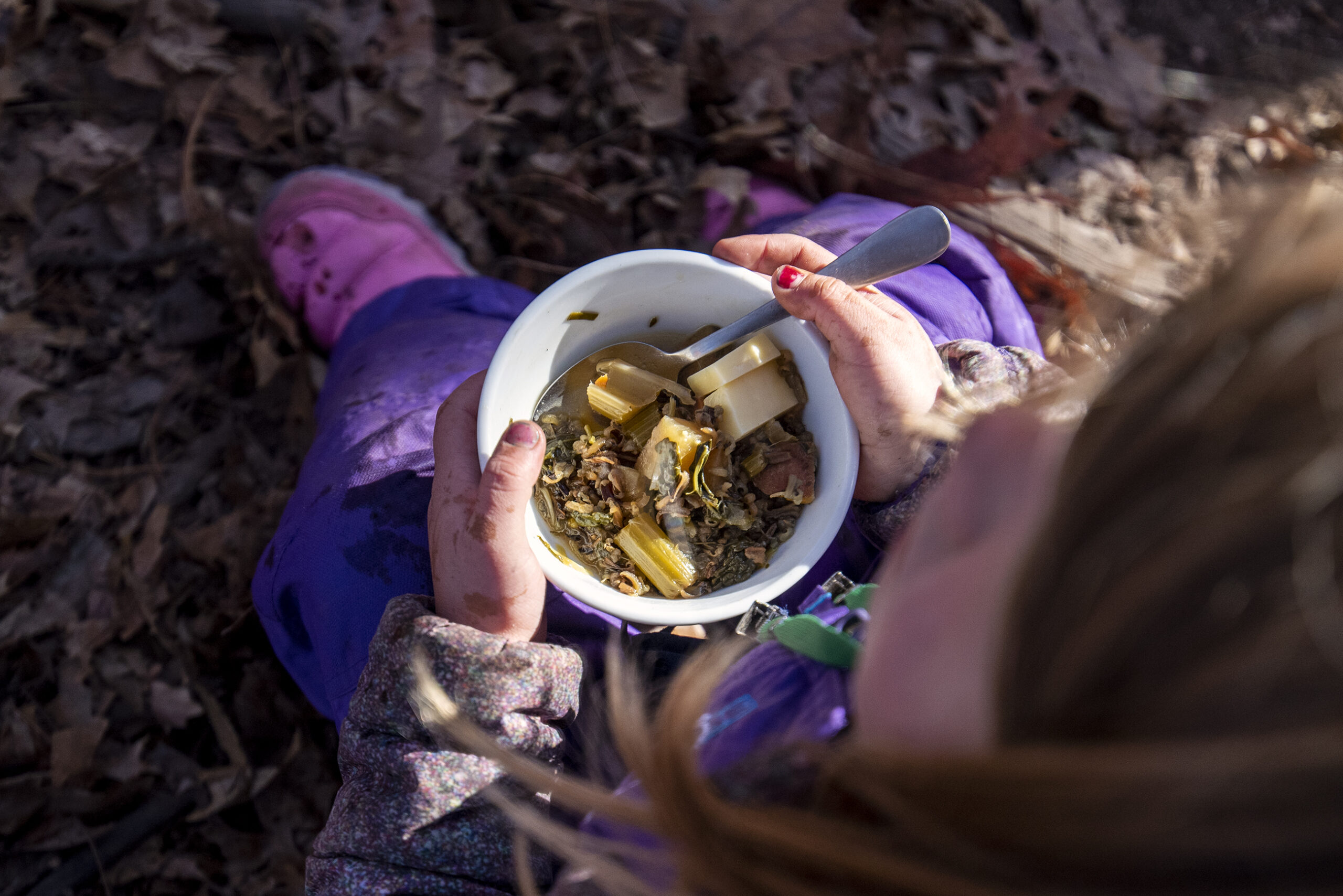 A bowl of soup can be seen from above as a small child holds it.