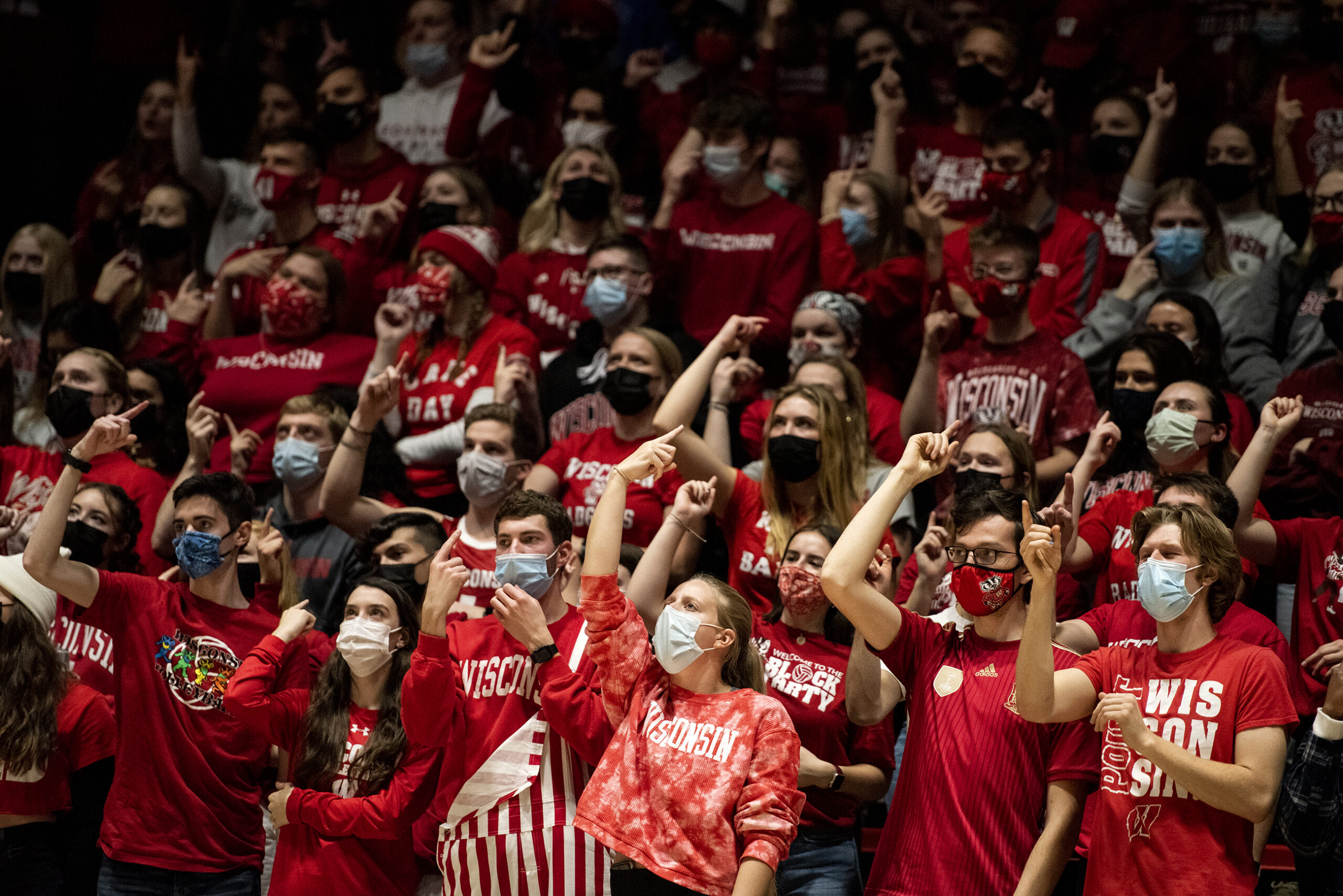 A sea of Wisconsin fans dressed in red raise their arms as they cheer.