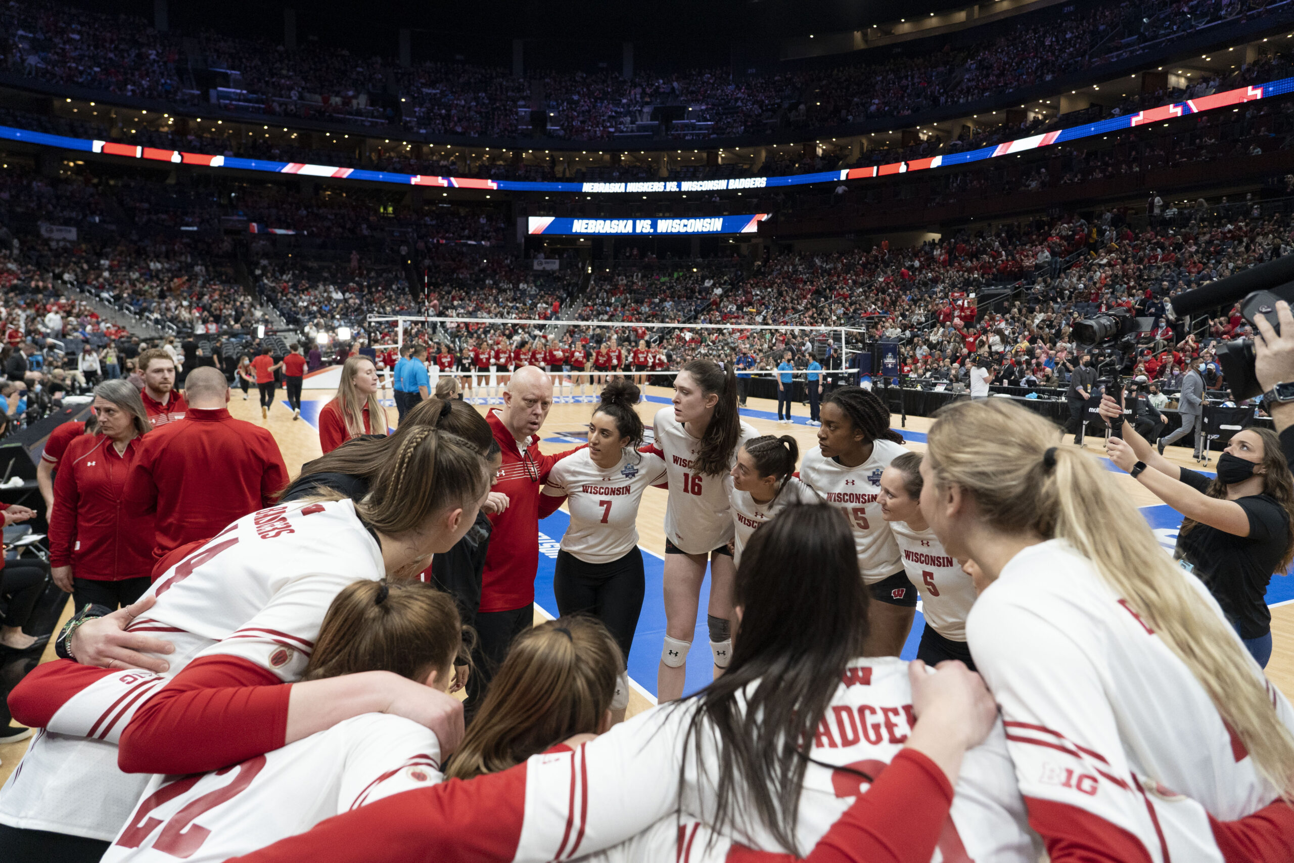 Badgers volleyball players huddle in a circle with coaches and team staff