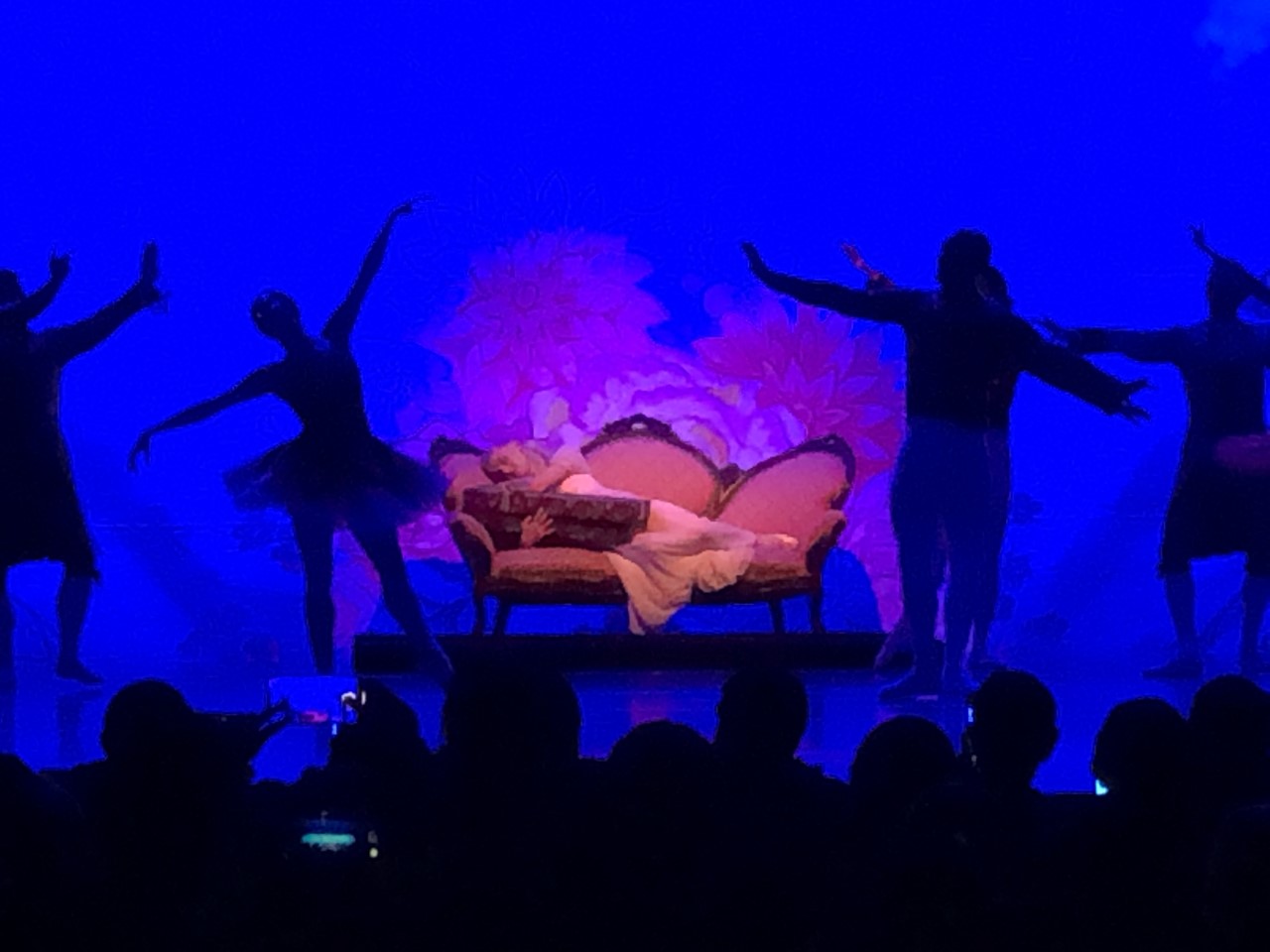 Dancers on stage surround another dancer on a couch during a performance of 