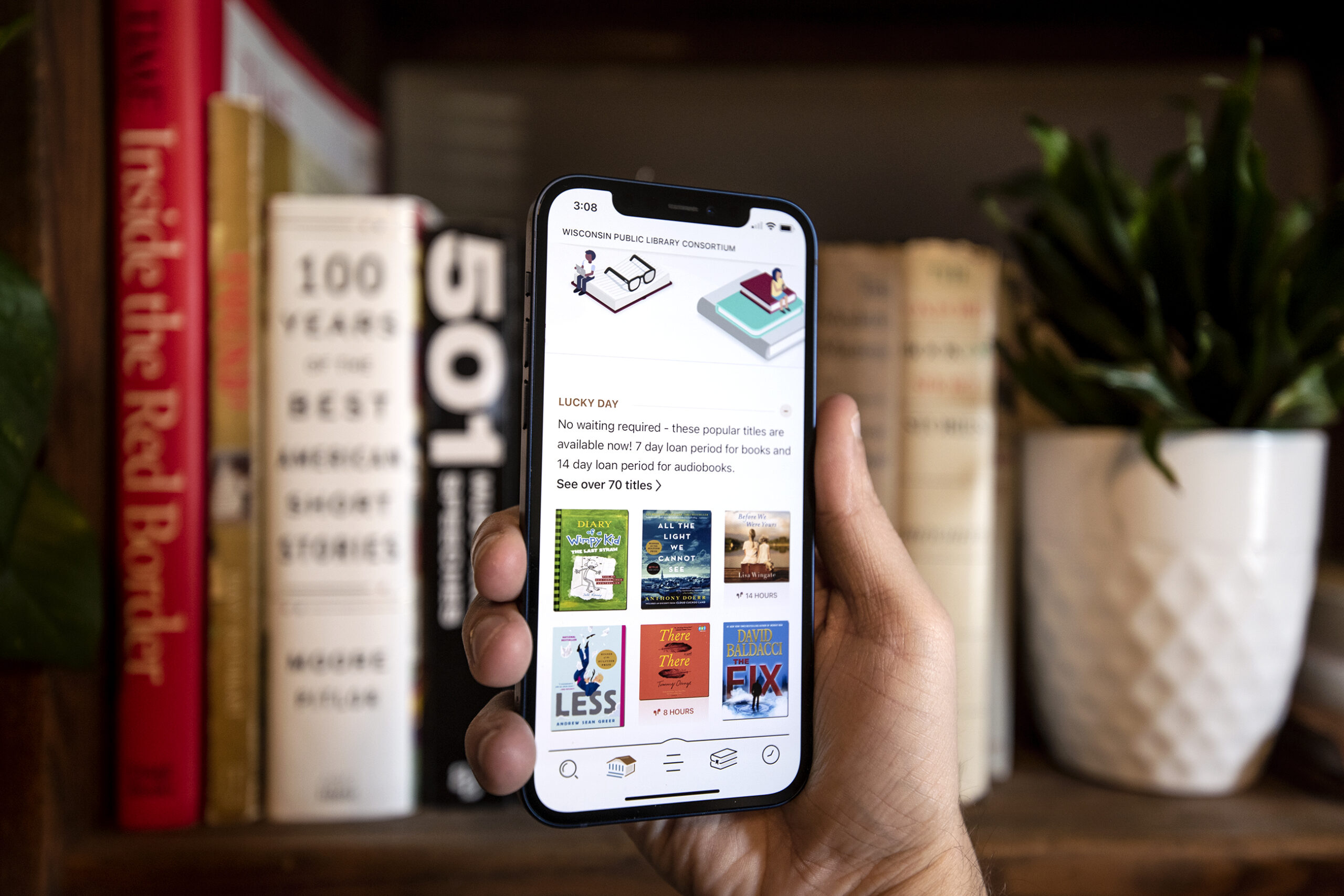 A phone showing an app with a collage of book covers is held in front of a book shelf