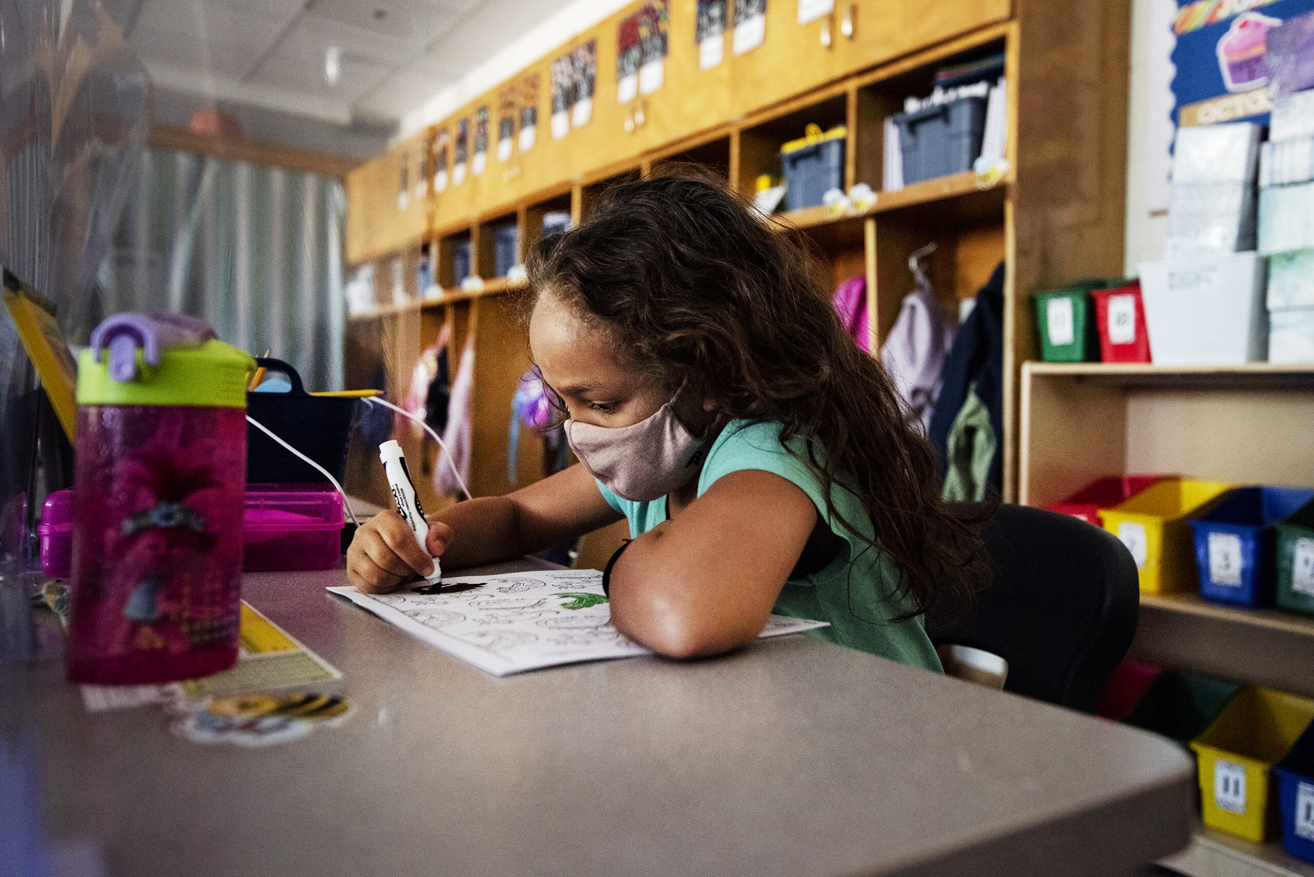 A girl wears a face mask as she colors a picture