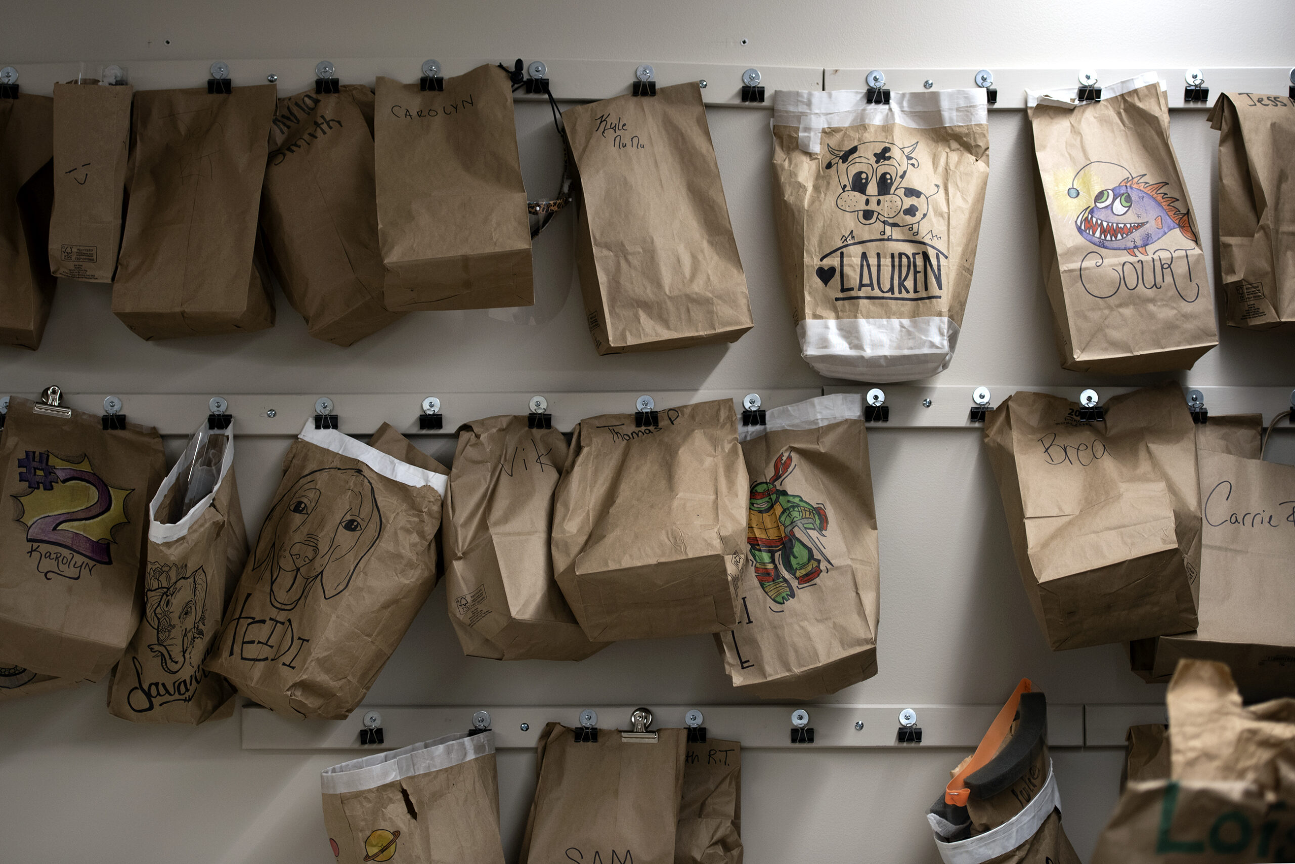 Brown paper bags with personalized drawings are hung on the wall in a hallway.