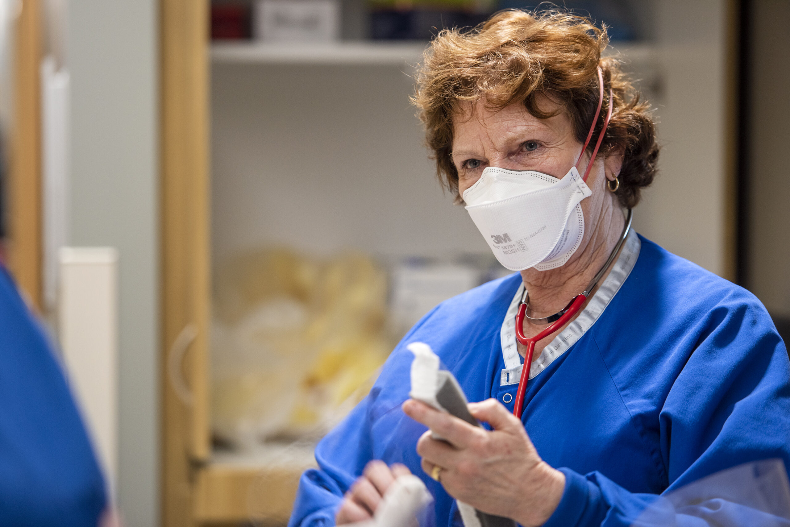 A nurse in blue scrubs cleans up after caring for a patient.