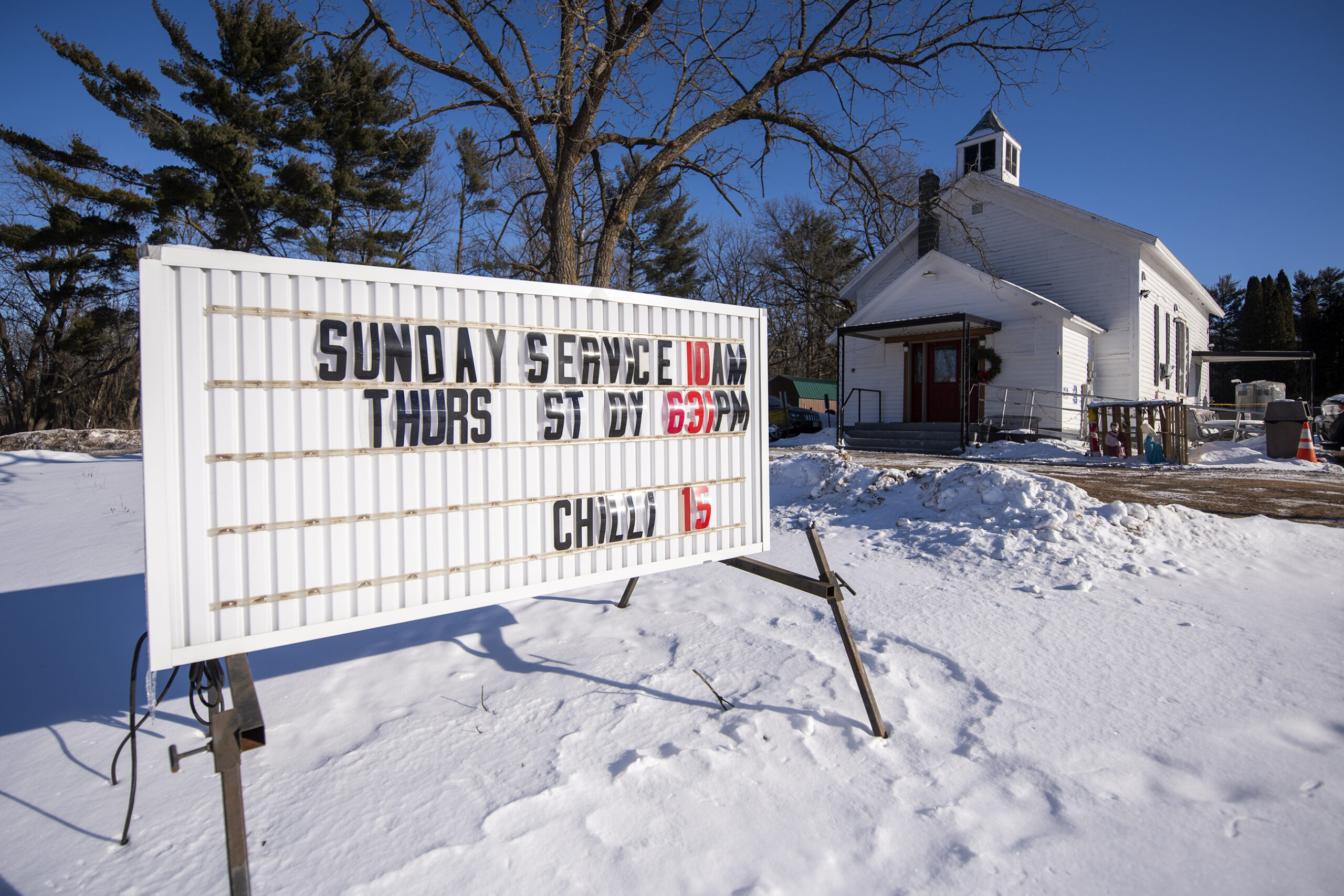 A white sign says what times church is held at the small white chapel.