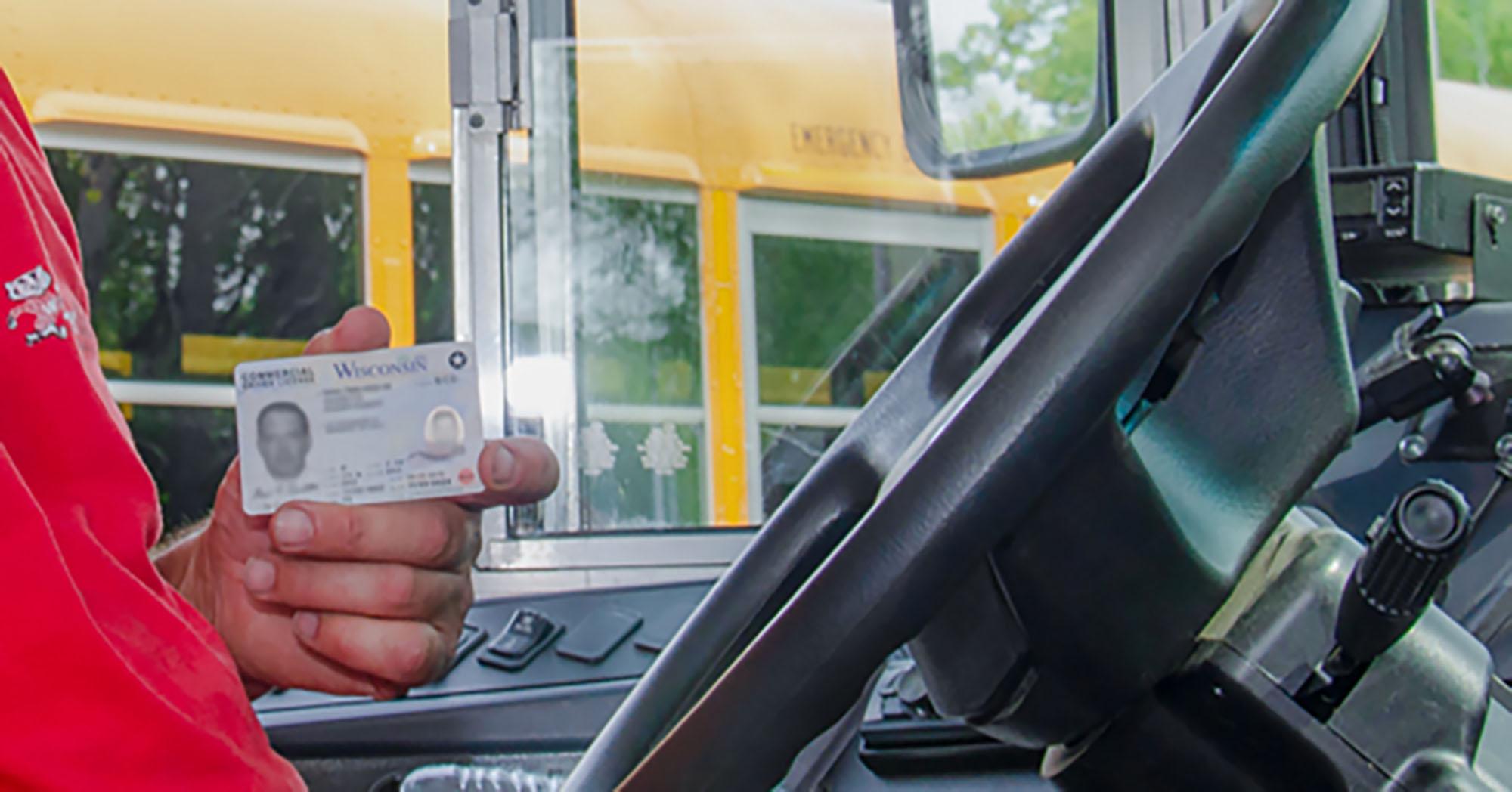 A bus driver holds their bus ID while in the driver's seat of a school bus