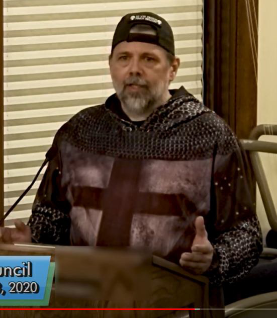 John Kraft wore a sweatshirt with a Templar cross and chainmail pattern while speaking at a public meeting in Hudson
