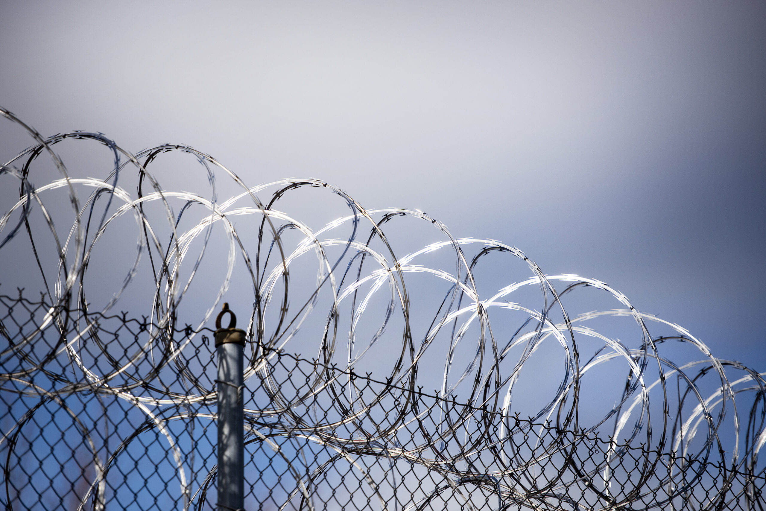 Light shines off of twisted barbed wire against the backdrop of a blue sky.