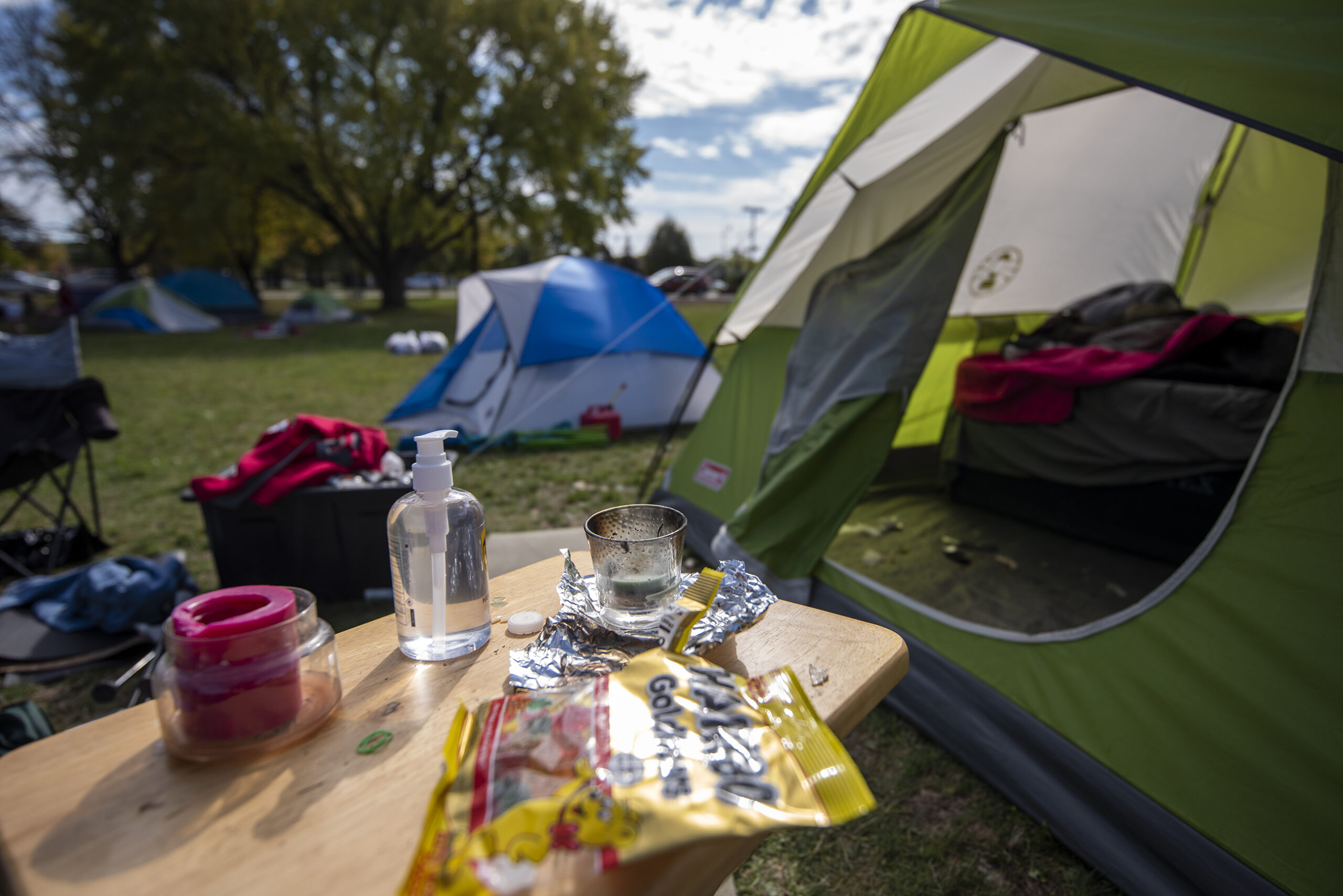 Hand sanitizer, a candle, and gummy bears can be seen on a TV tray outside of a green tent.