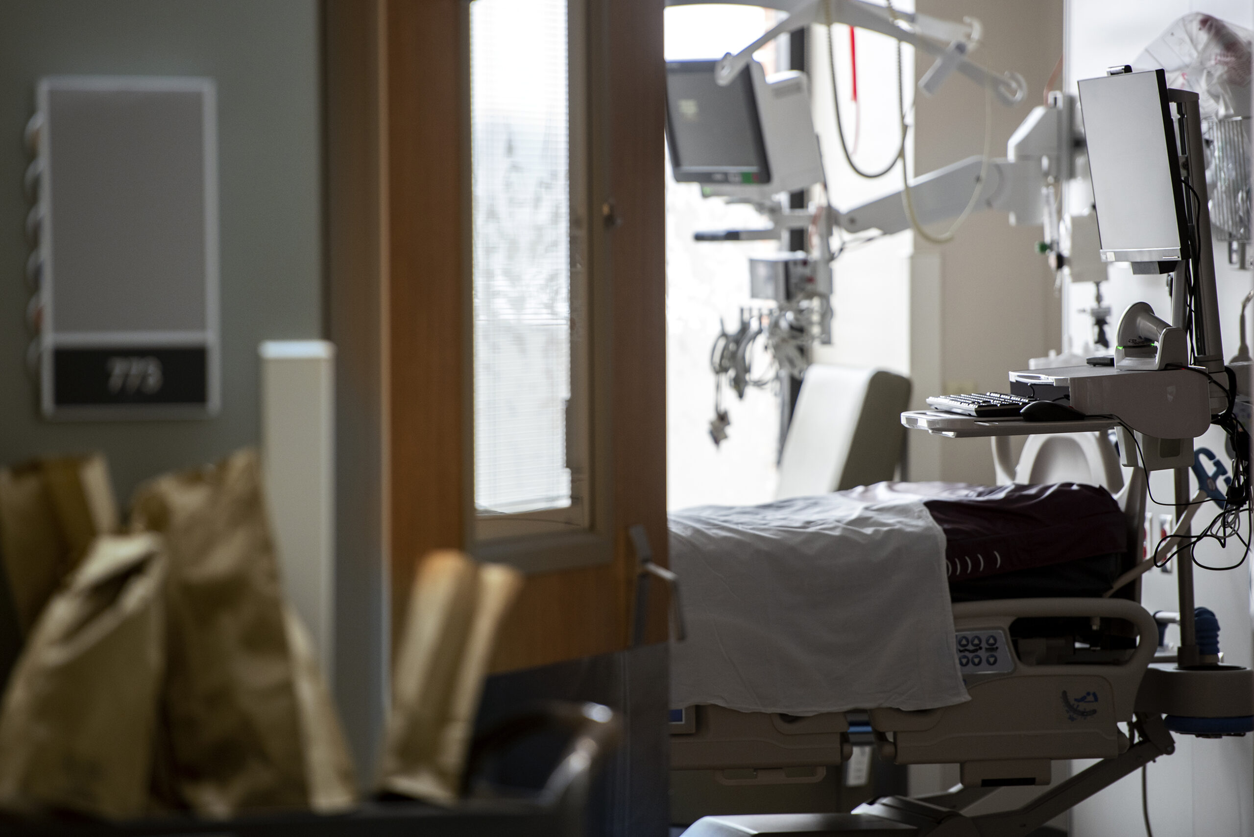 An empty hospital bed is seen through a doorway.