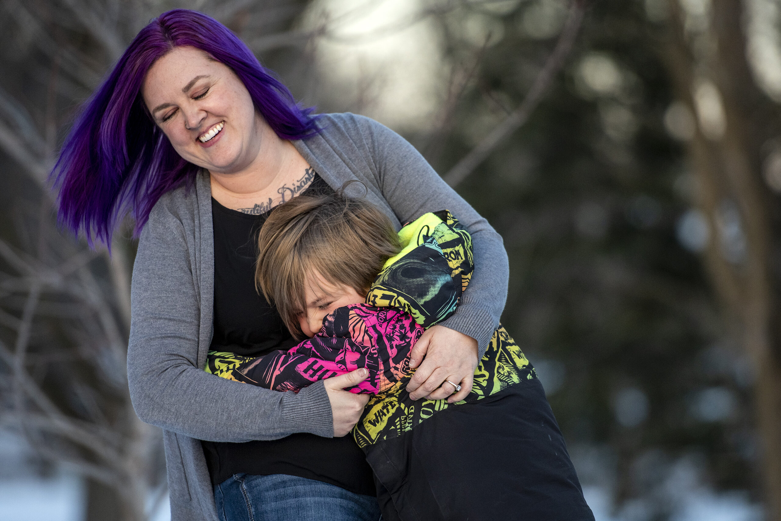 A mother and son smile as they hug each other outside.