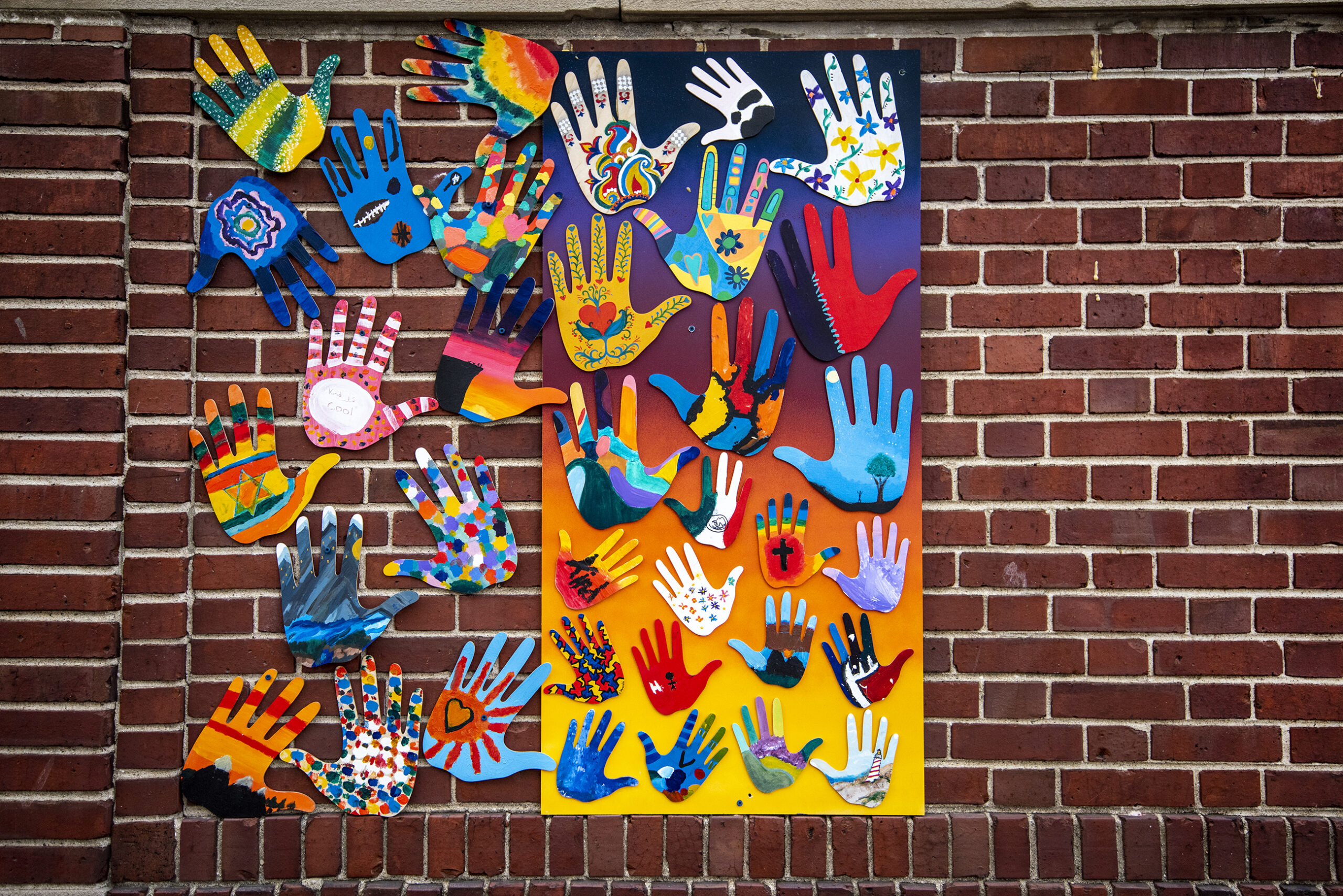 A painting of hands as bright colors is displayed on a brick wall.