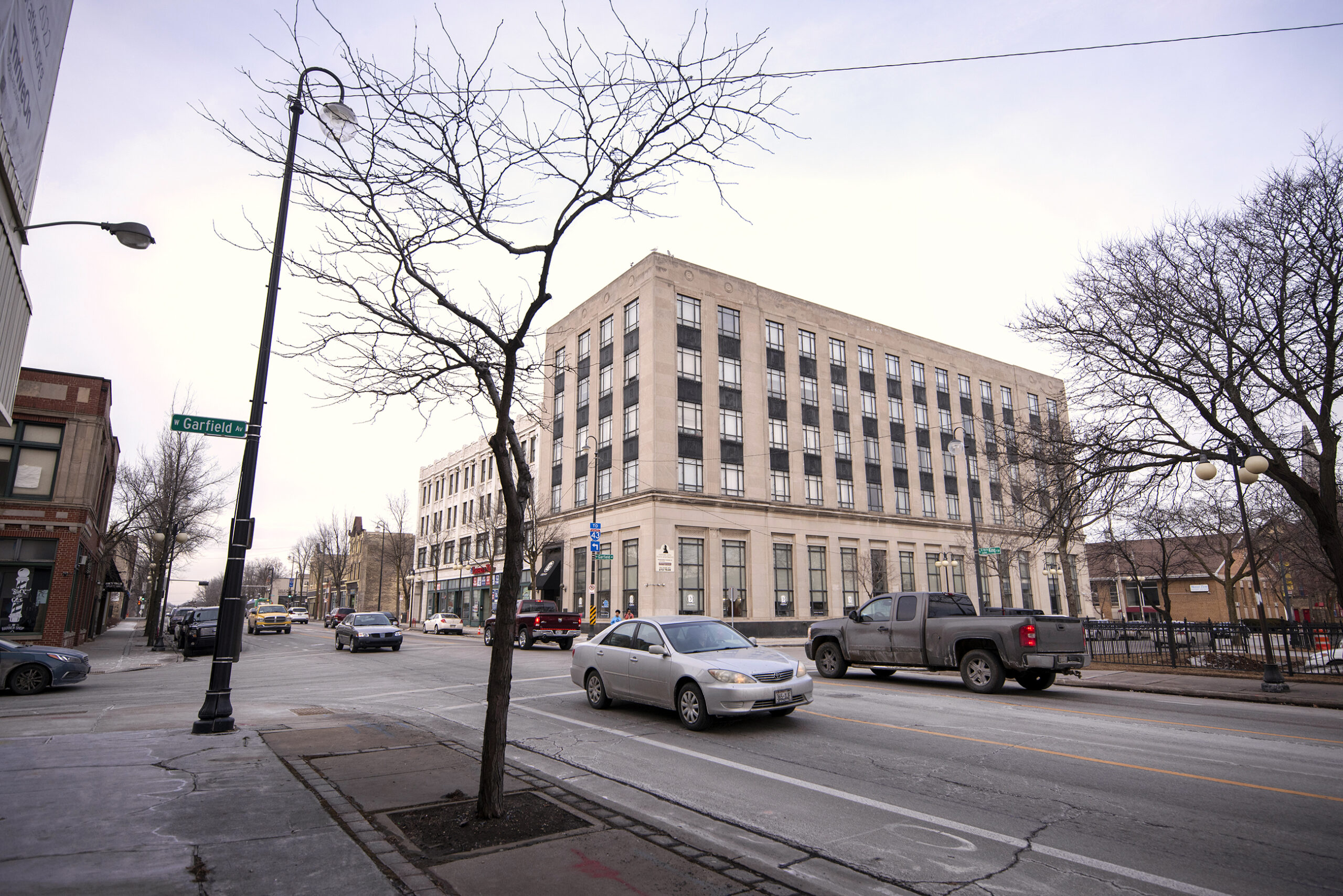 A silver car passes a beige building.