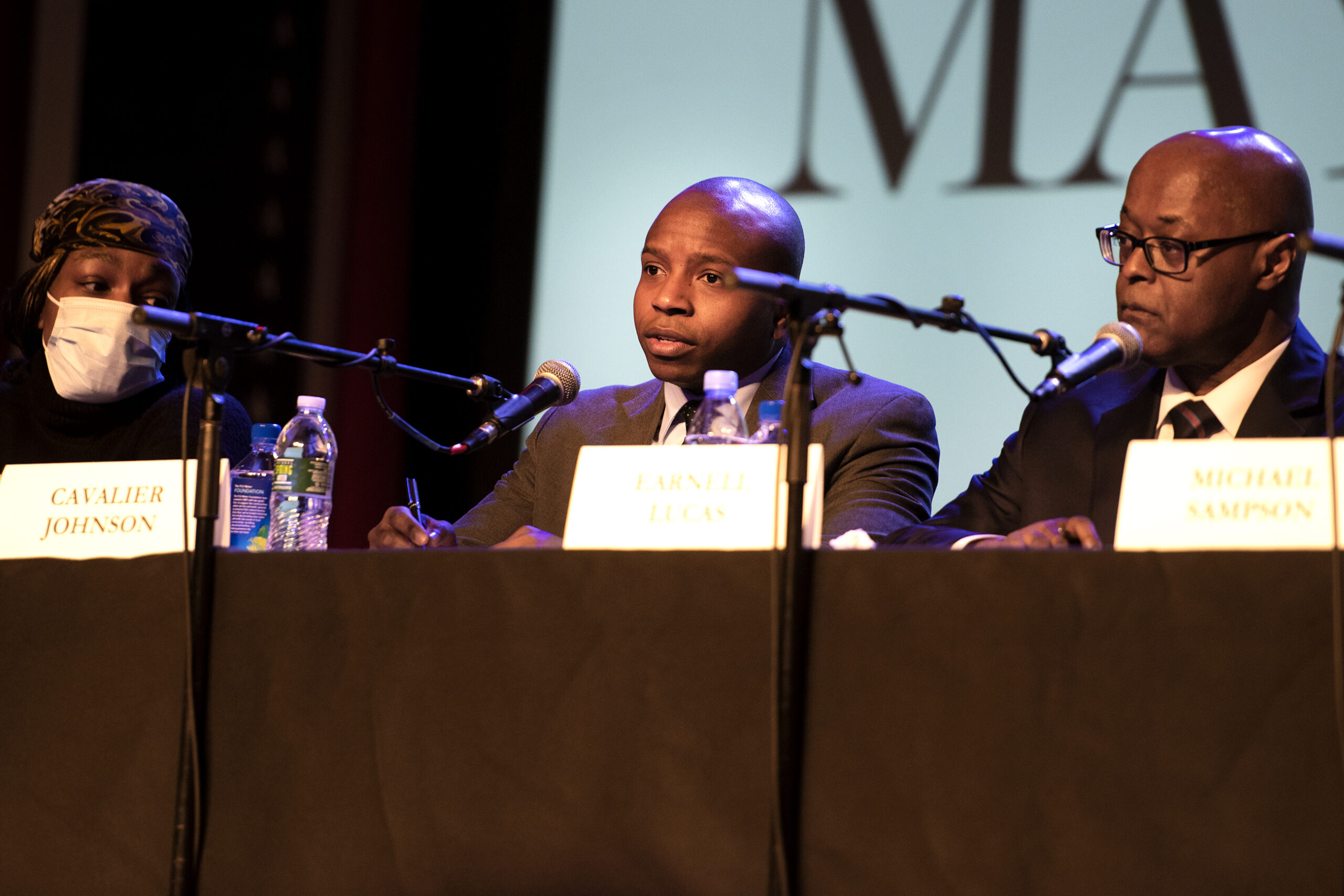 A candidate speaks into a microphone from a theater stage.