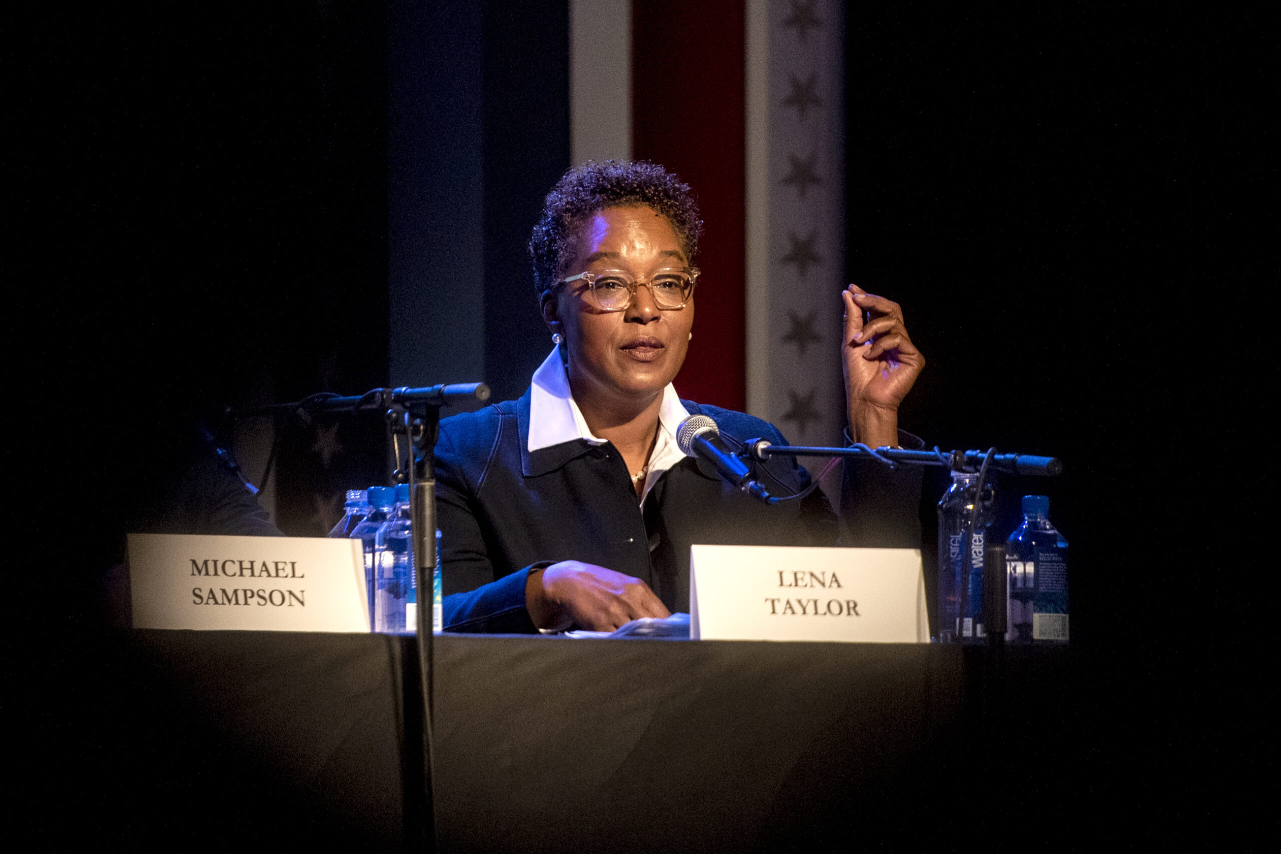 Sen. Lena Taylor can be seen through heads in the crowd as she gestures while asking a question.