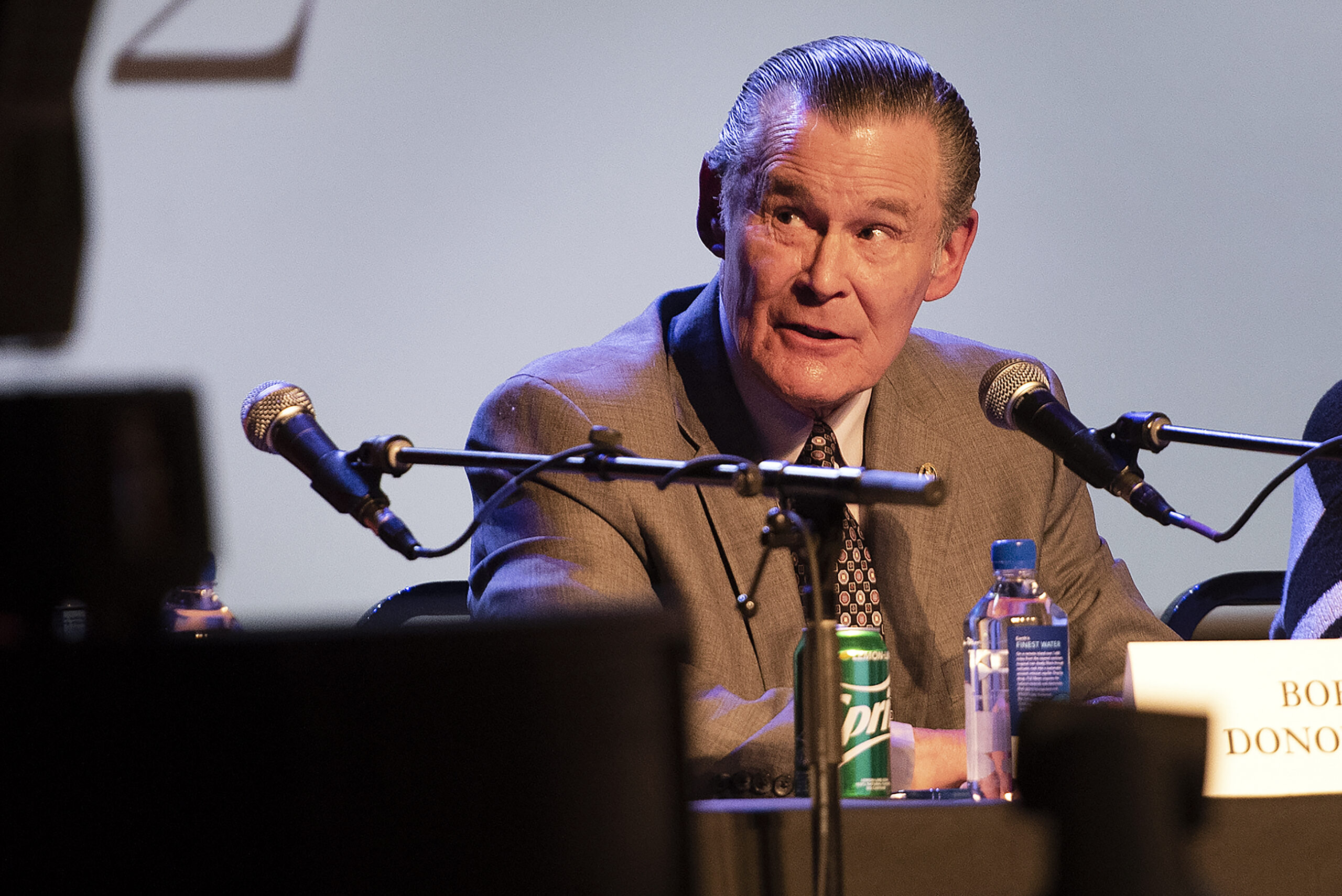 A candidate speaks into a microphone during a forum on a theater stage.