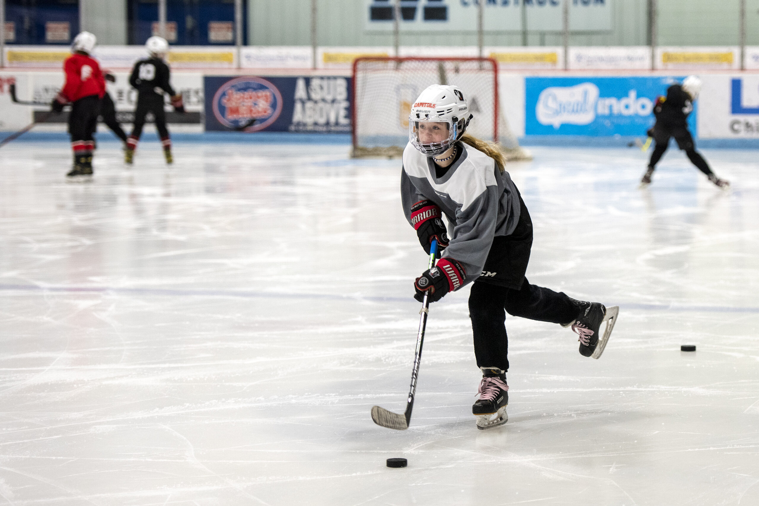 A girl in hockey gear moves a puck across the ice.