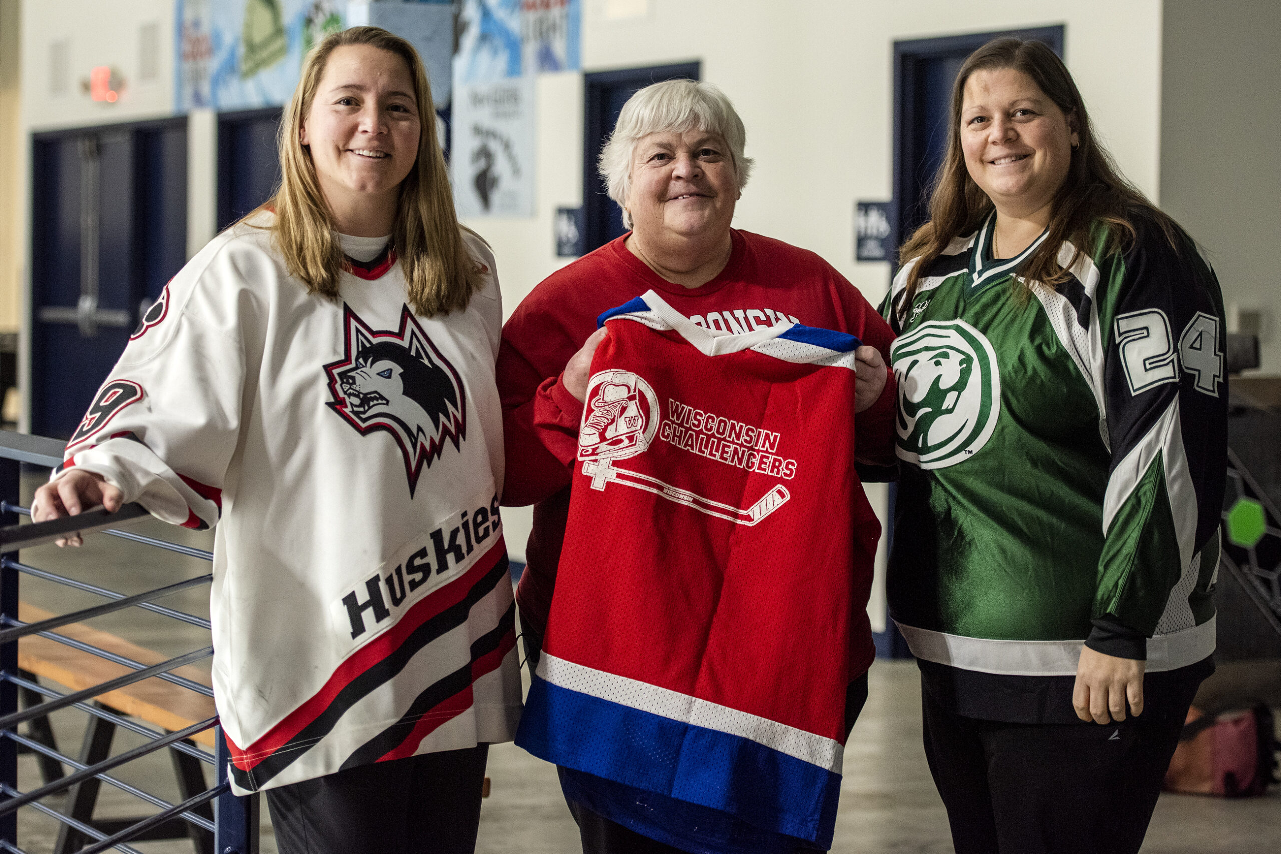 Three women stand together in a hockey rink.