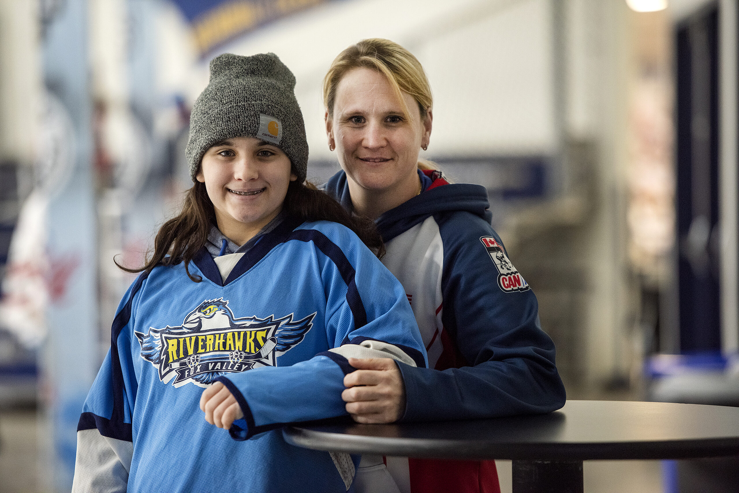 A woman stands with her daughter at a hockey rink.